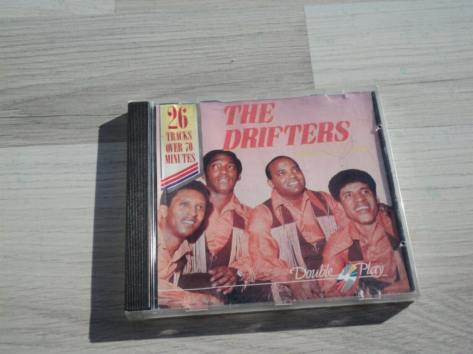 音樂 桌布 壁紙 — 一個The Drifters的復古CD盒放在淺色木質表面上，顯示了樂團的笑臉和'Double Play'品牌標誌。
