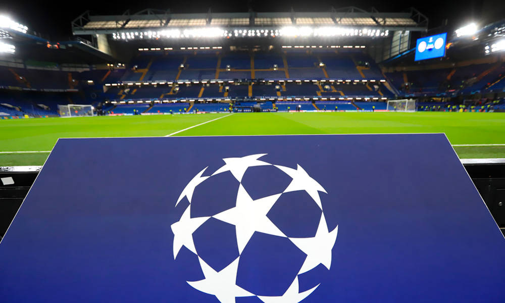 bridge 桌布 壁紙 — 一個UEFA歐冠標誌醒目地放在一個藍色板上，前面是一個空無一人、燈火通明的足球場，在夜晚時分。