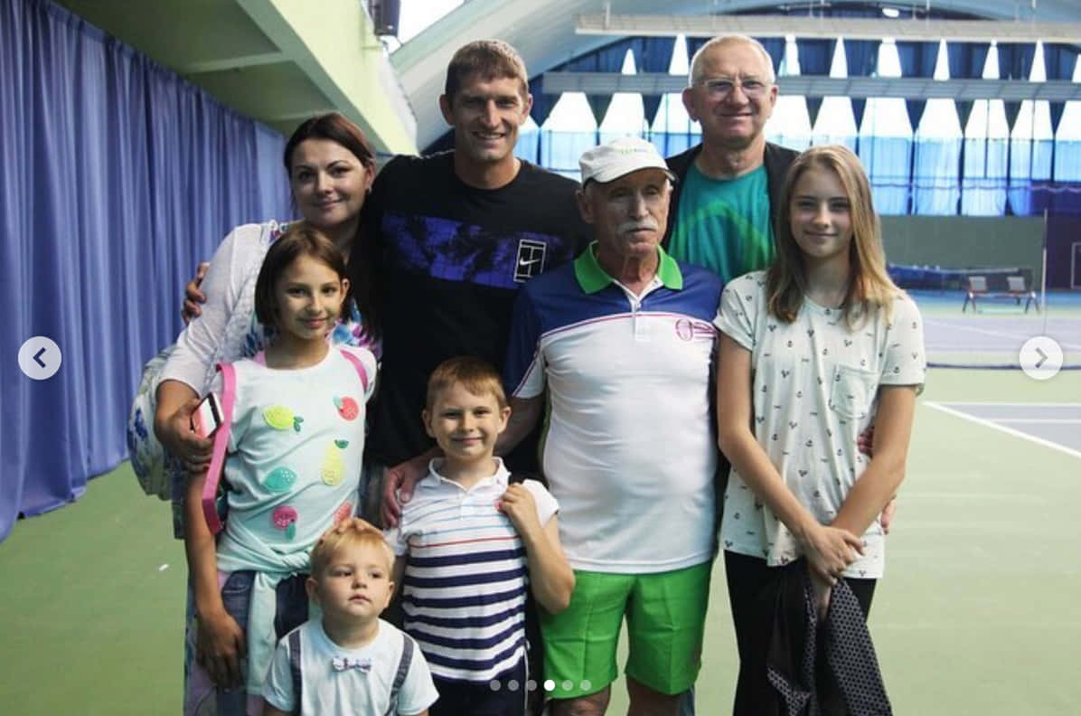 Tennis 桌布 壁紙 — 一個七人家庭在一個有藍色窗簾和綠色地板的室內網球場上一起擺姿勢。