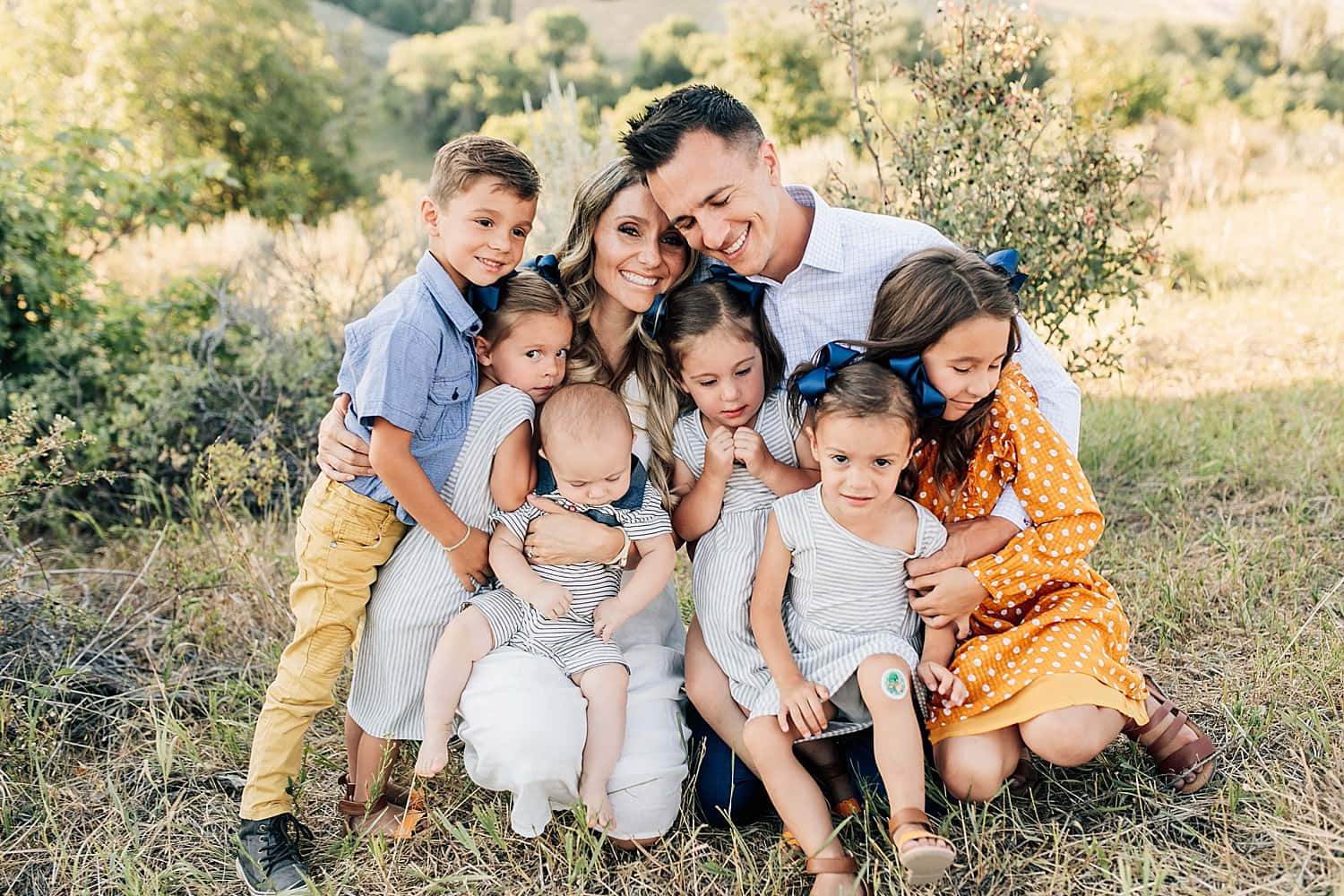 Family 桌布 壁紙 — 一個七人微笑家庭在陽光明媚的草地上緊密地擺姿勢，背景有樹木。