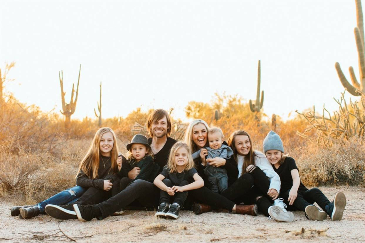 Family 桌布 壁紙 — 一個七人微笑家庭坐在沙漠地上，背景是高聳的薩瓜羅仙人掌和溫暖的金色日落天空。