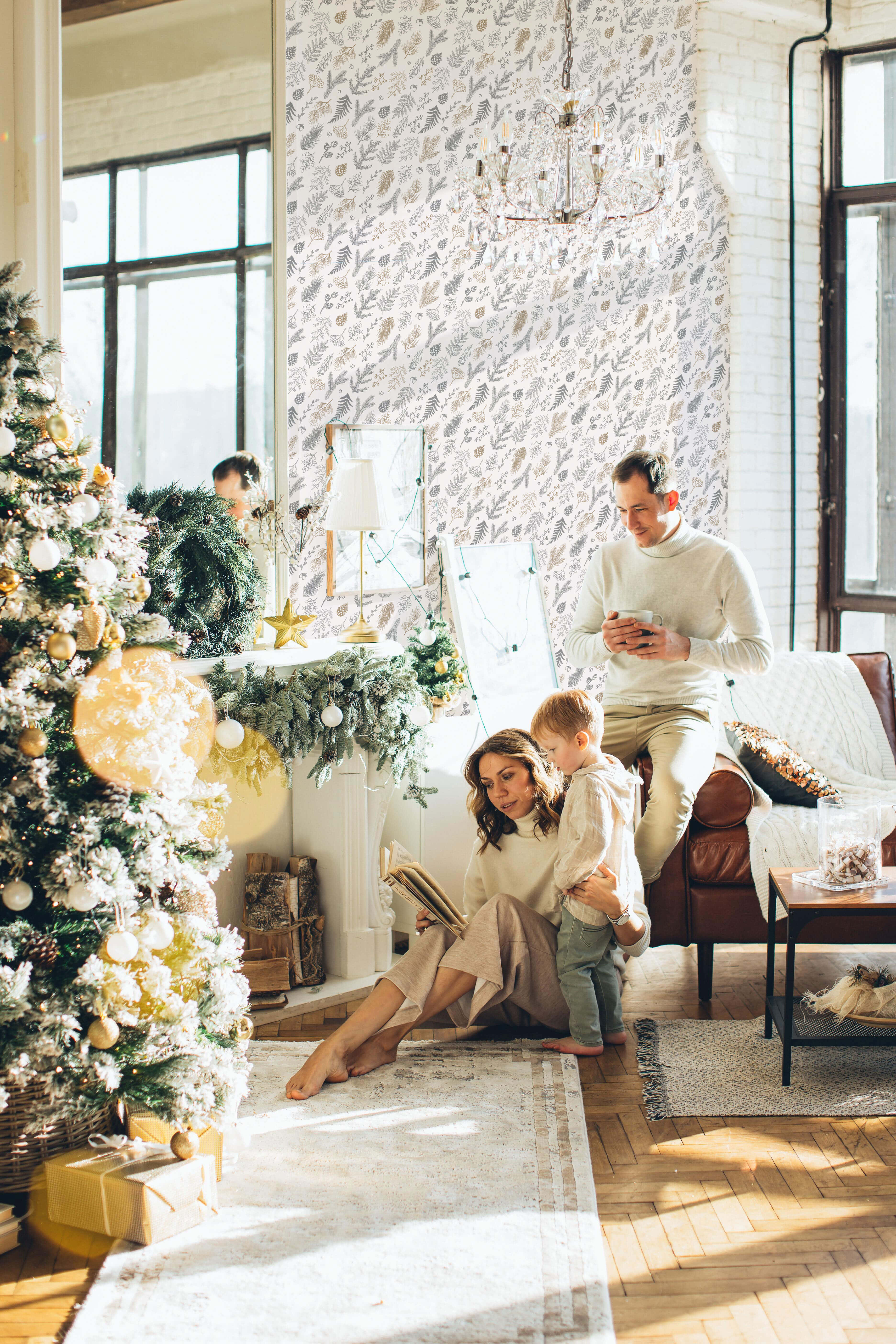 Christmas Living Room 桌布 壁紙 — 一個三人家庭在陽光充足的現代客廳中，在裝飾好的聖誕樹旁享受舒適的節日時光。