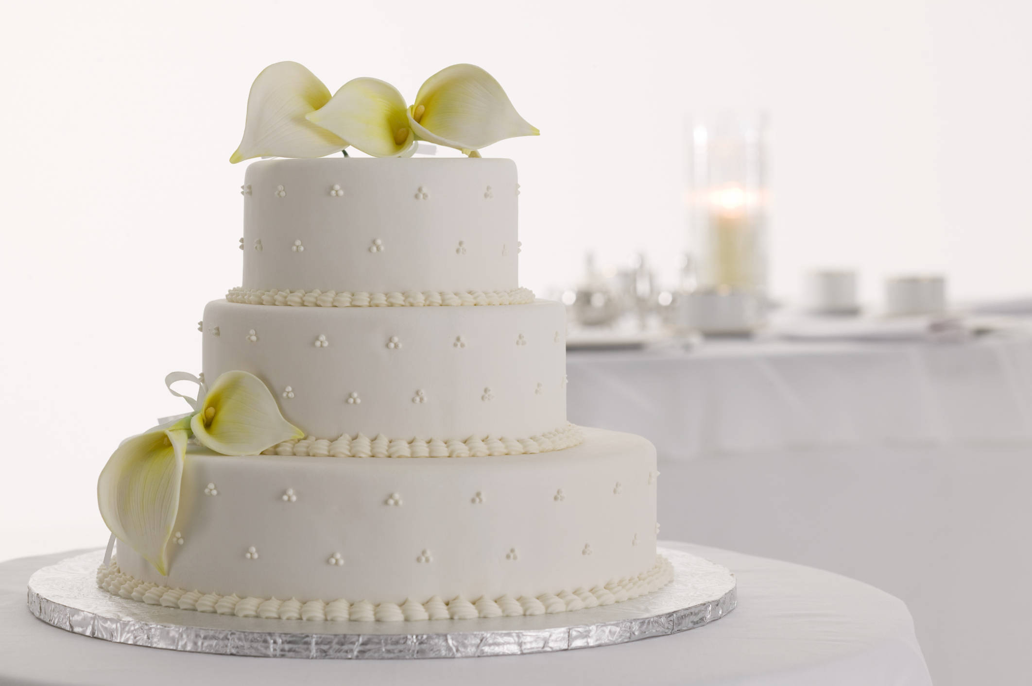 蛋糕 桌布 壁紙 — 一個三層白色結婚蛋糕，飾以精緻的馬蹄蓮和圓點，優雅地放置在銀色支架上。