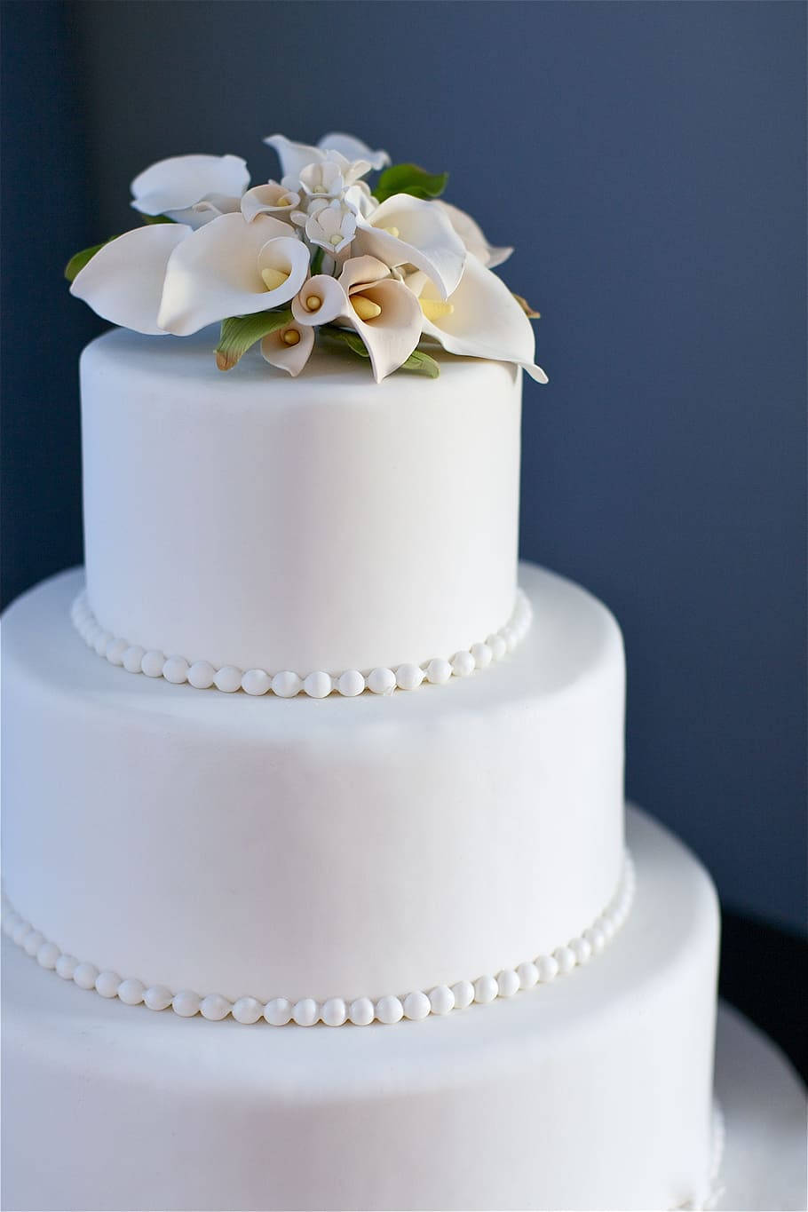 Wedding 桌布 壁紙 — 一個三層白色結婚蛋糕，飾以馬蹄蓮和珍珠般的珠飾，背景為深藍色。
