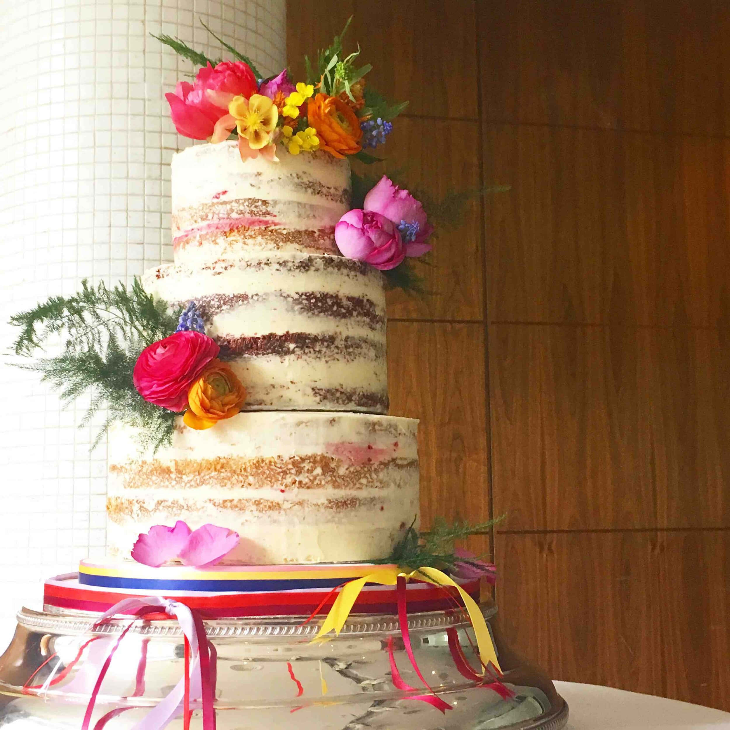 Cake Fondant 桌布 壁紙 — 一個三層裸體結婚蛋糕，飾以鮮豔的鮮花和彩色絲帶，置於銀色支架上。