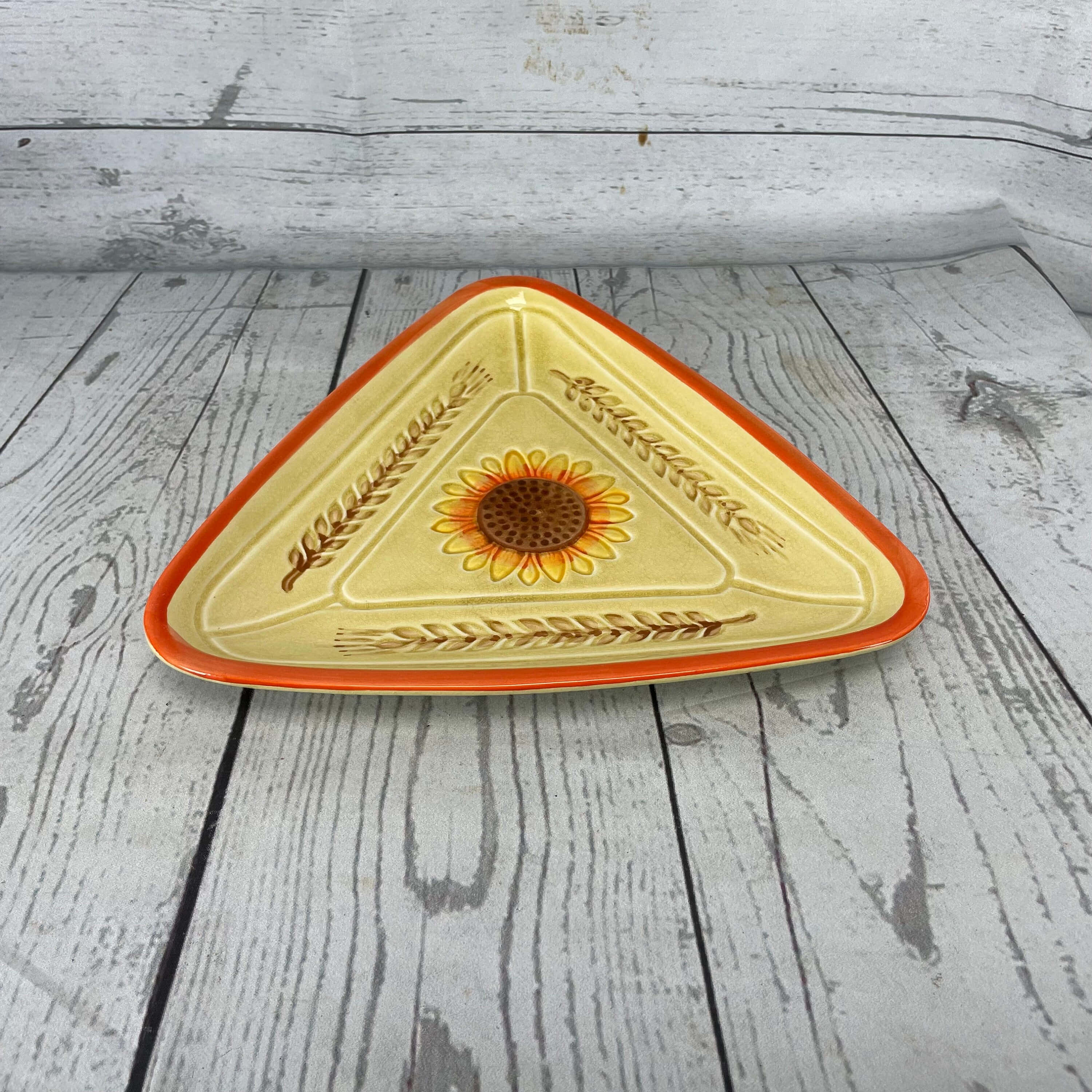 Yellow Triangle 桌布 壁紙 — 一個三角形陶瓷盤，帶有向日葵和小麥圖案，放置在風化的白色木板上。