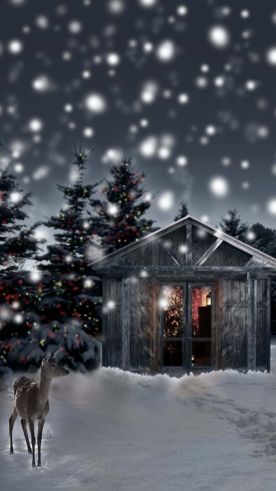 鹿 桌布 壁紙 — 一個下雪的冬夜場景，一隻鹿站在一間在飄落的雪花下溫暖發光的質樸木屋前。