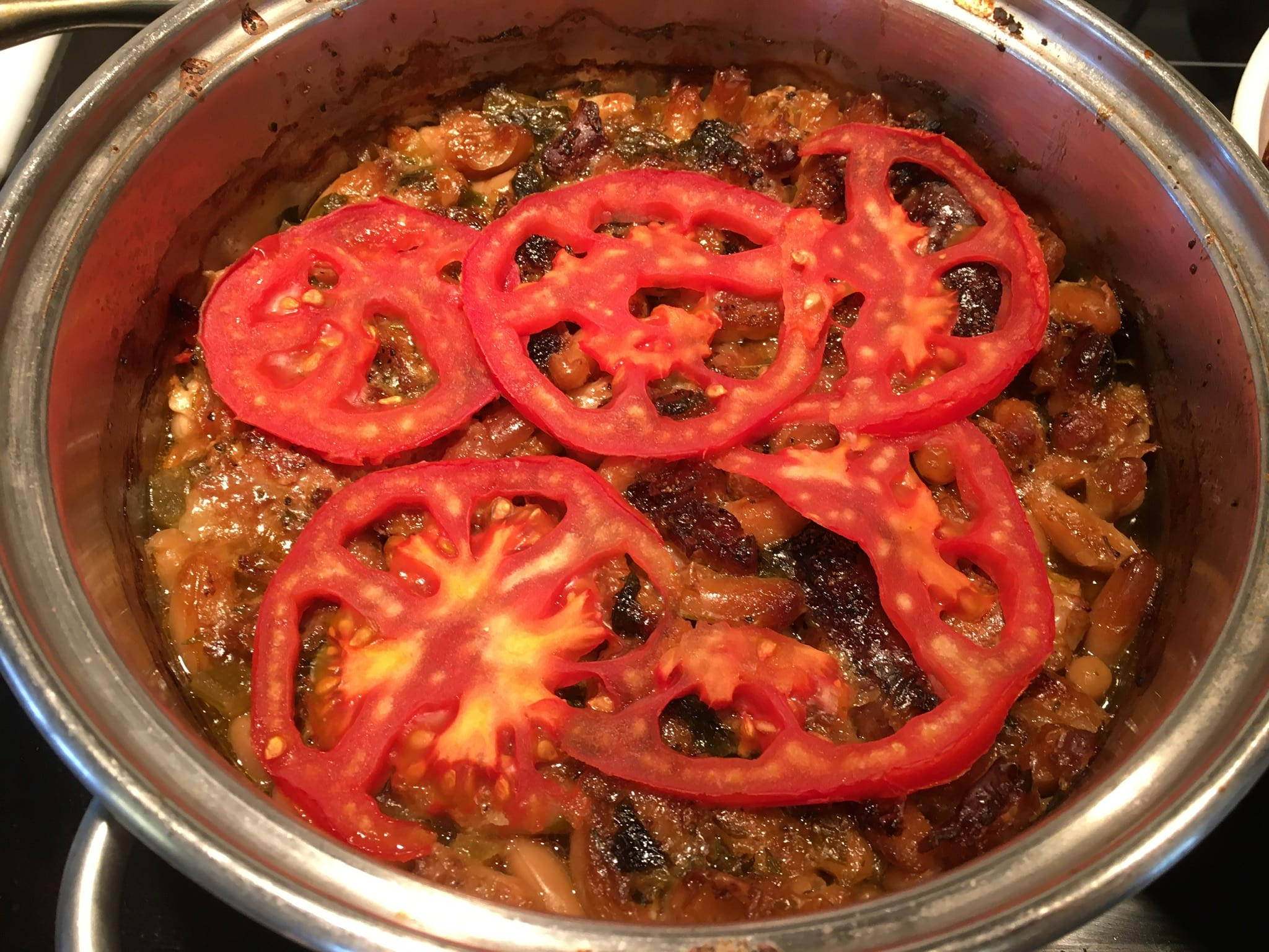 yummy 桌布 壁紙 — 一個不鏽鋼鍋盛載著濃郁的燉菜，上面鋪滿鮮紅的番茄片，露出多汁的內部。