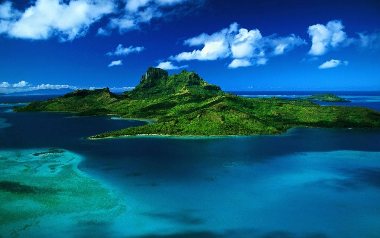 Mauritius 桌布 壁紙 — 一個中央有山的茂密綠色島嶼的鳥瞰圖，周圍環繞著充滿活力的碧綠海水和深藍色海洋，天空明亮，有蓬鬆的白雲。