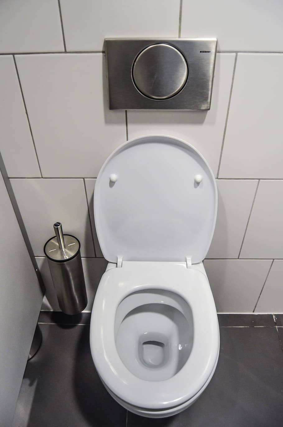 Toilet 桌布 壁紙 — 一個乾淨的白色馬桶，蓋子打開，位於現代瓷磚浴室中，配有不鏽鋼沖水板和馬桶刷。