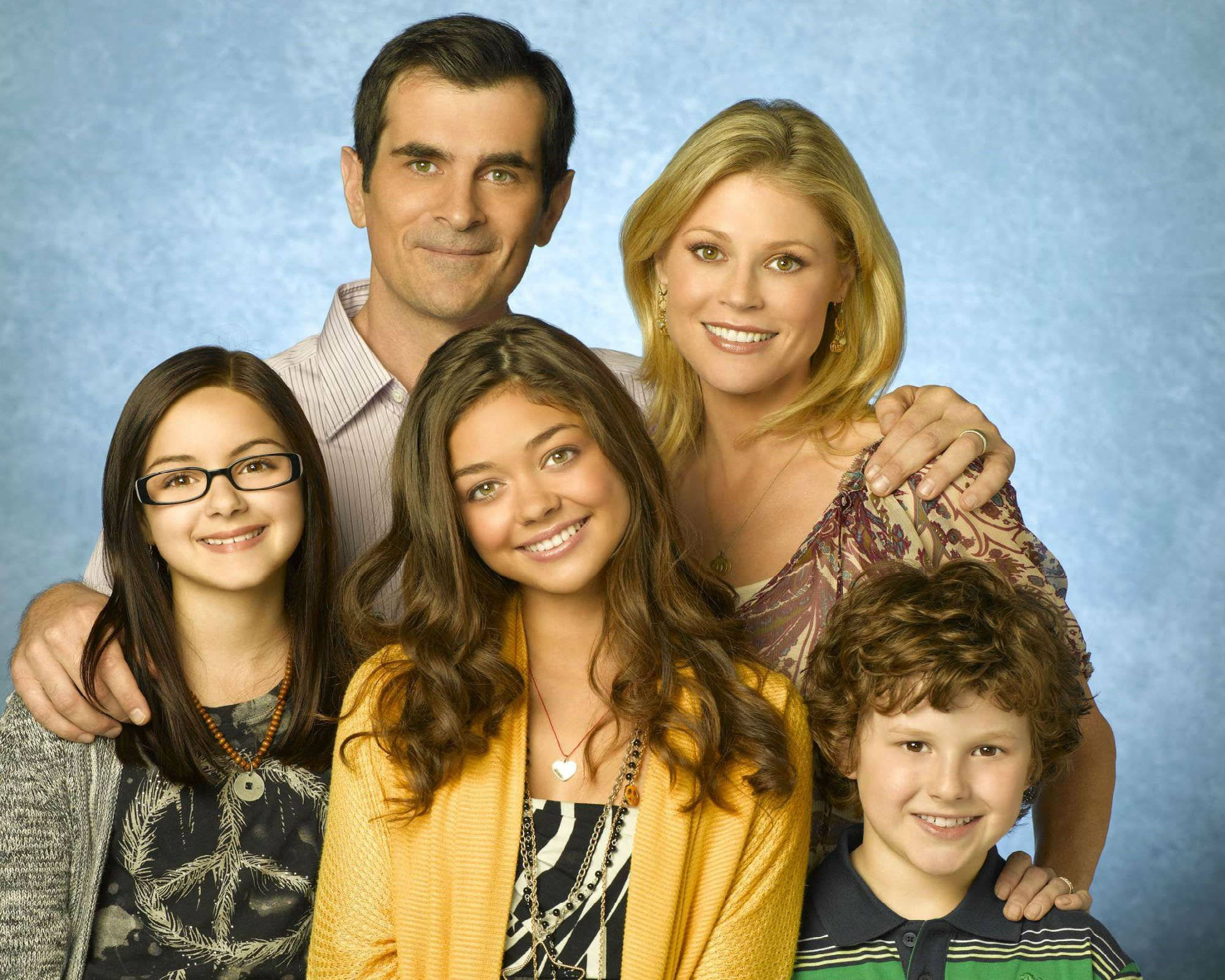 Modern Family 桌布 壁紙 — 一個五口之家微笑著緊密地靠在一起，背景是帶有紋理的藍色攝影棚背景。