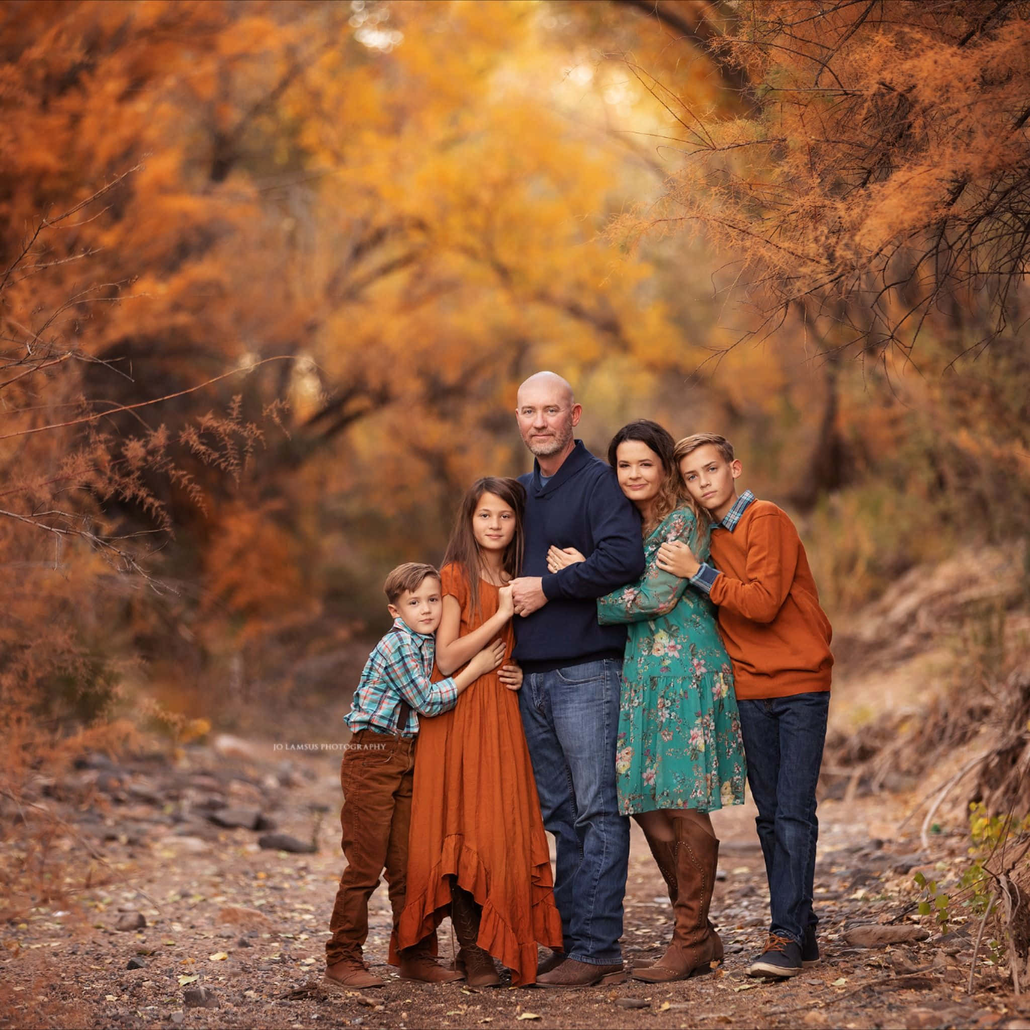 Family 桌布 壁紙 — 一個五口之家站在一條落葉覆蓋的小路上，上方是充滿活力的橙色秋樹樹冠。