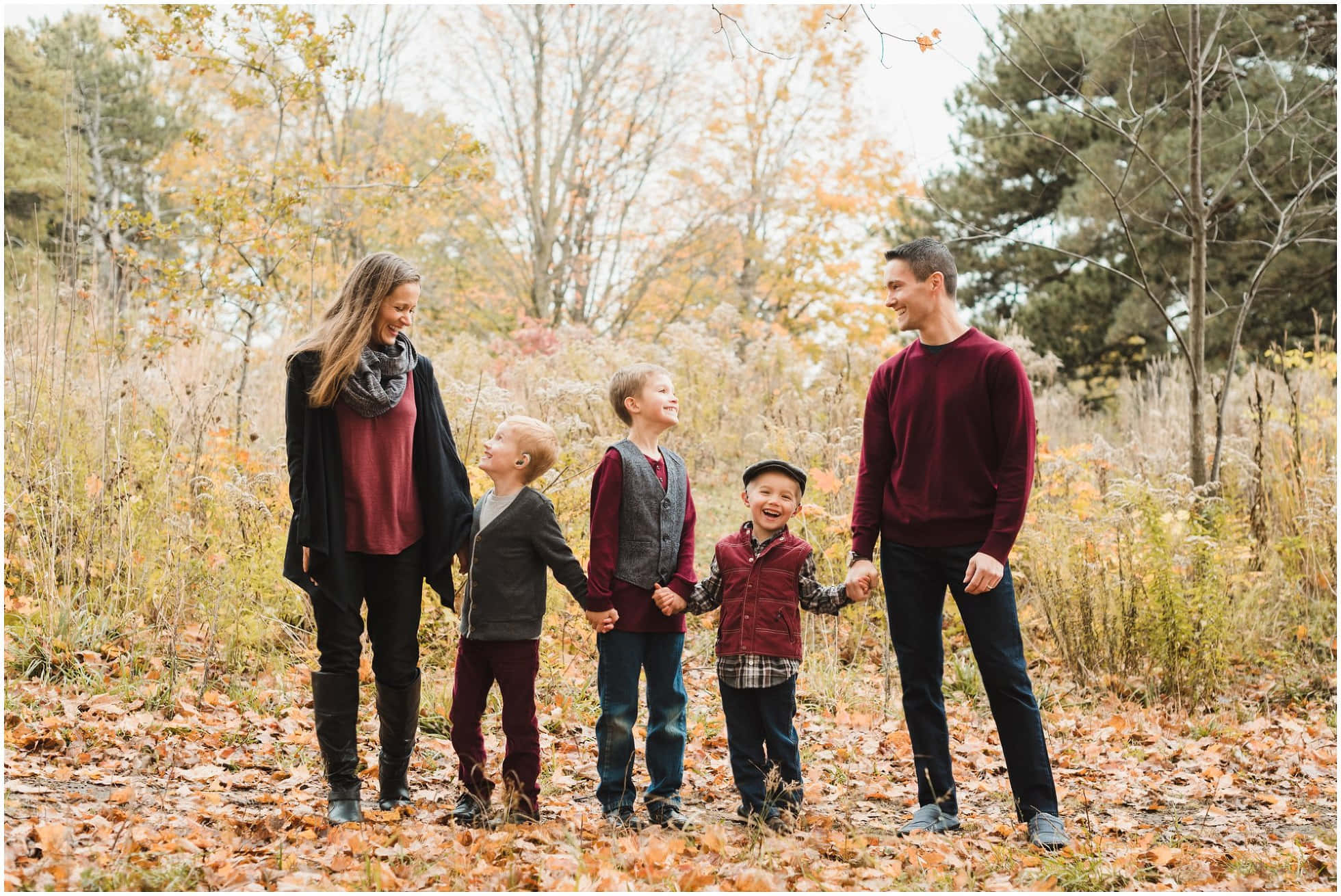 Fall Family 桌布 壁紙 — 一個五口之家面帶微笑，手牽手站在鋪滿金色秋葉的森林中。