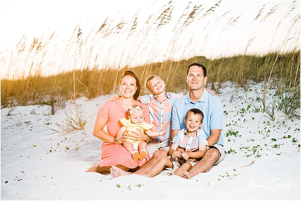 Beach Family 桌布 壁紙 — 一個五口幸福家庭在日落時分坐在陽光普照的海灘上，身後高高的草叢隨風搖曳。