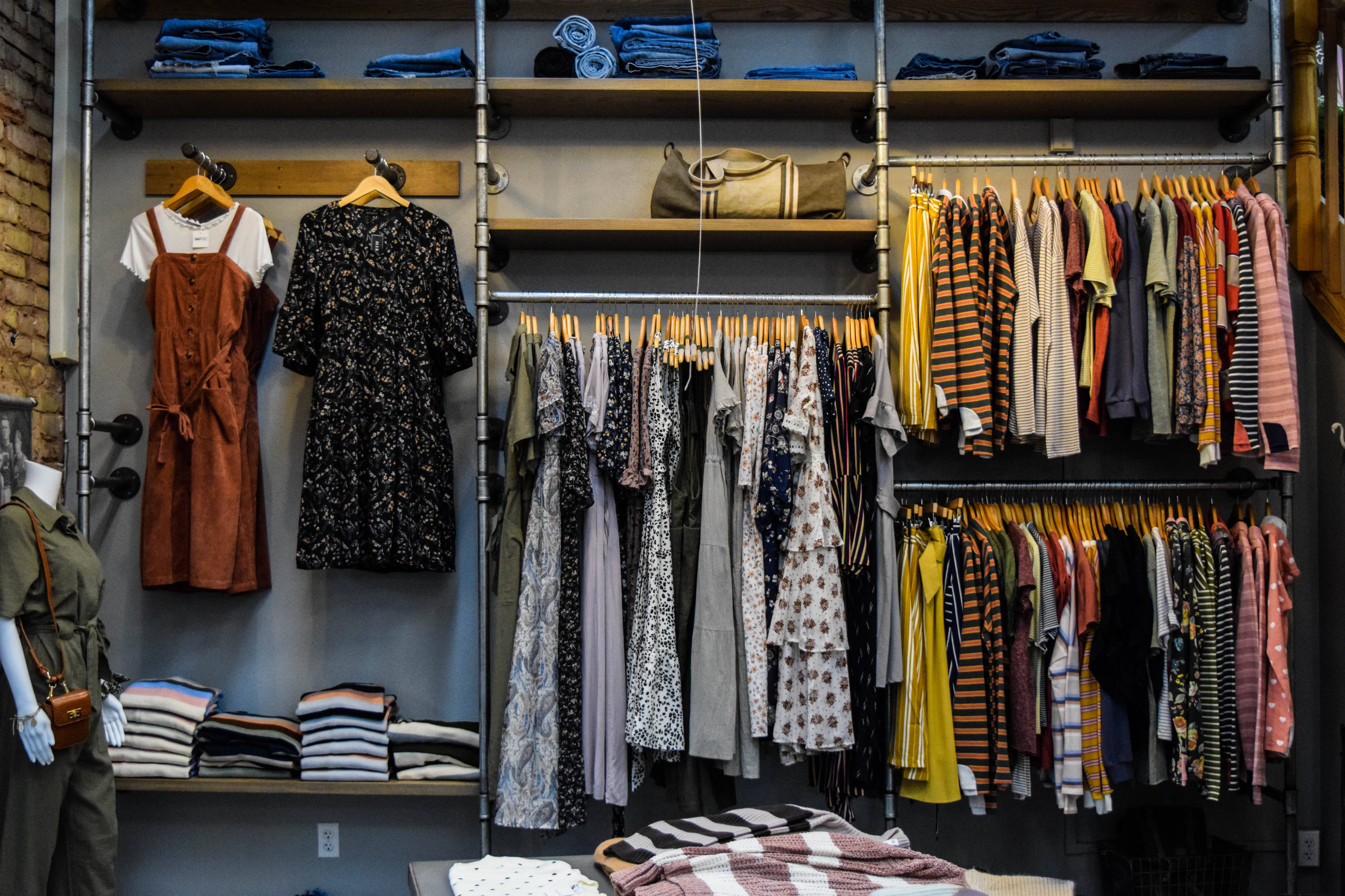Trendy 桌布 壁紙 — 一個井然有序的精品衣櫃展示色彩繽紛的摺疊和懸掛衣物，放在工業貨架上，背景是磚牆。