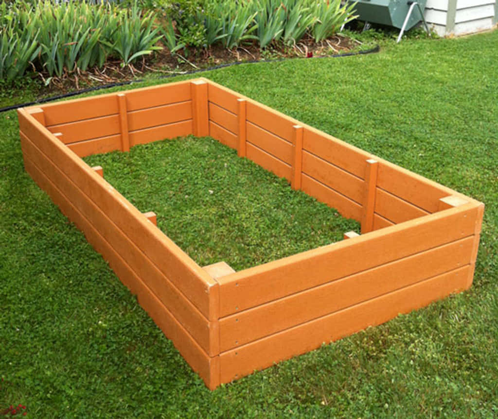 Garden Bed 桌布 壁紙 — 一個亮橙色木製高架花園床空置在茂密的綠色草坪上，周圍有高大的綠色植物。
