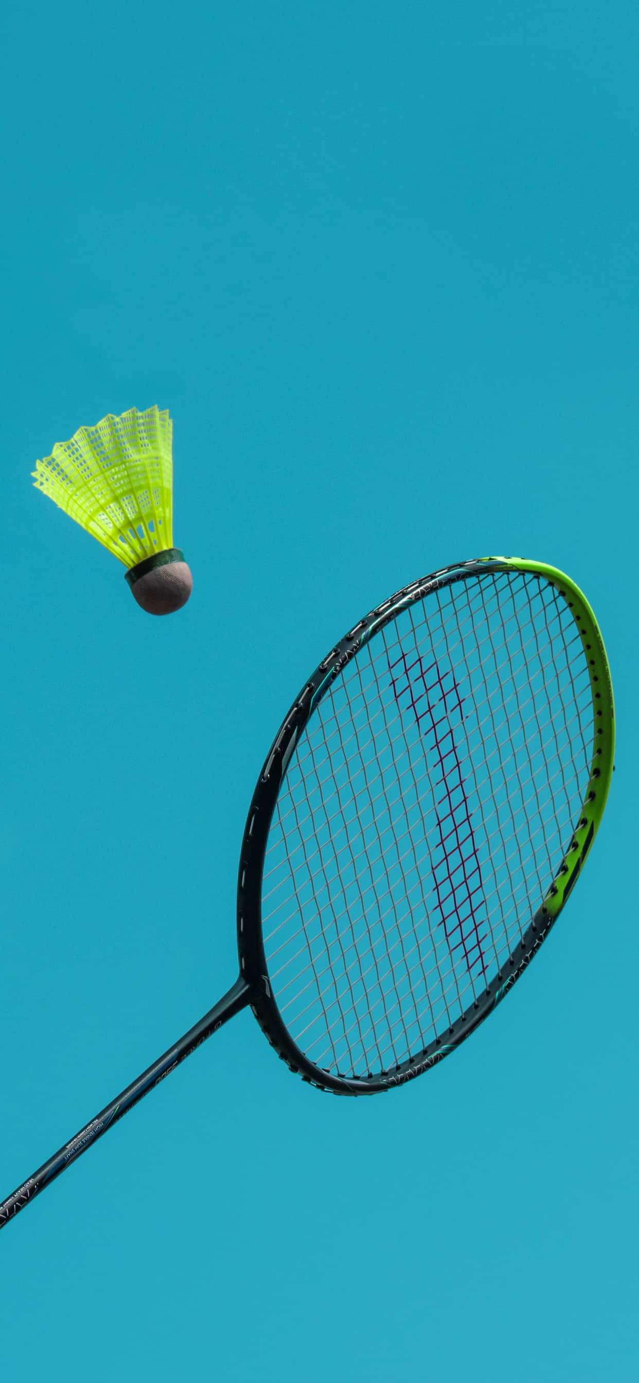 iPhone Xs Max Badminton 桌布 壁紙 — 一個亮眼的螢光黃色羽毛球在半空中懸浮，旁邊是一把黑色和綠色的羽毛球拍，背景是純色的青綠色天空。