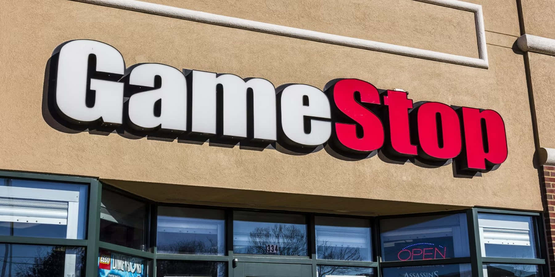 GameStop 桌布 壁紙 — 一個亮紅色和白色的GameStop商店招牌，安裝在米色建築物外牆上，在晴朗的日光下。