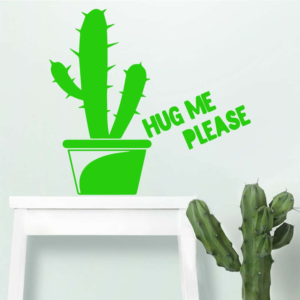 Kawaii Cactus 桌布 壁紙 — 一個亮綠色仙人掌牆貼，上面有「HUG ME PLEASE」字樣，位於白色層架上的一個真實仙人掌上方，背景是素色牆壁。