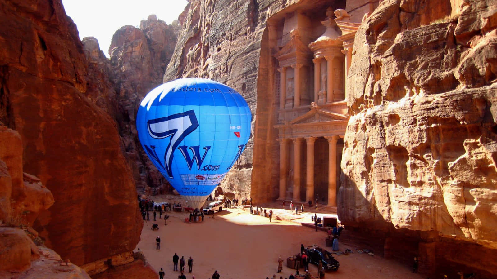 Hot Air Balloon 桌布 壁紙 — 一個亮藍色的熱氣球漂浮在佩特拉標誌性寶庫旁高聳的砂岩懸崖之間。