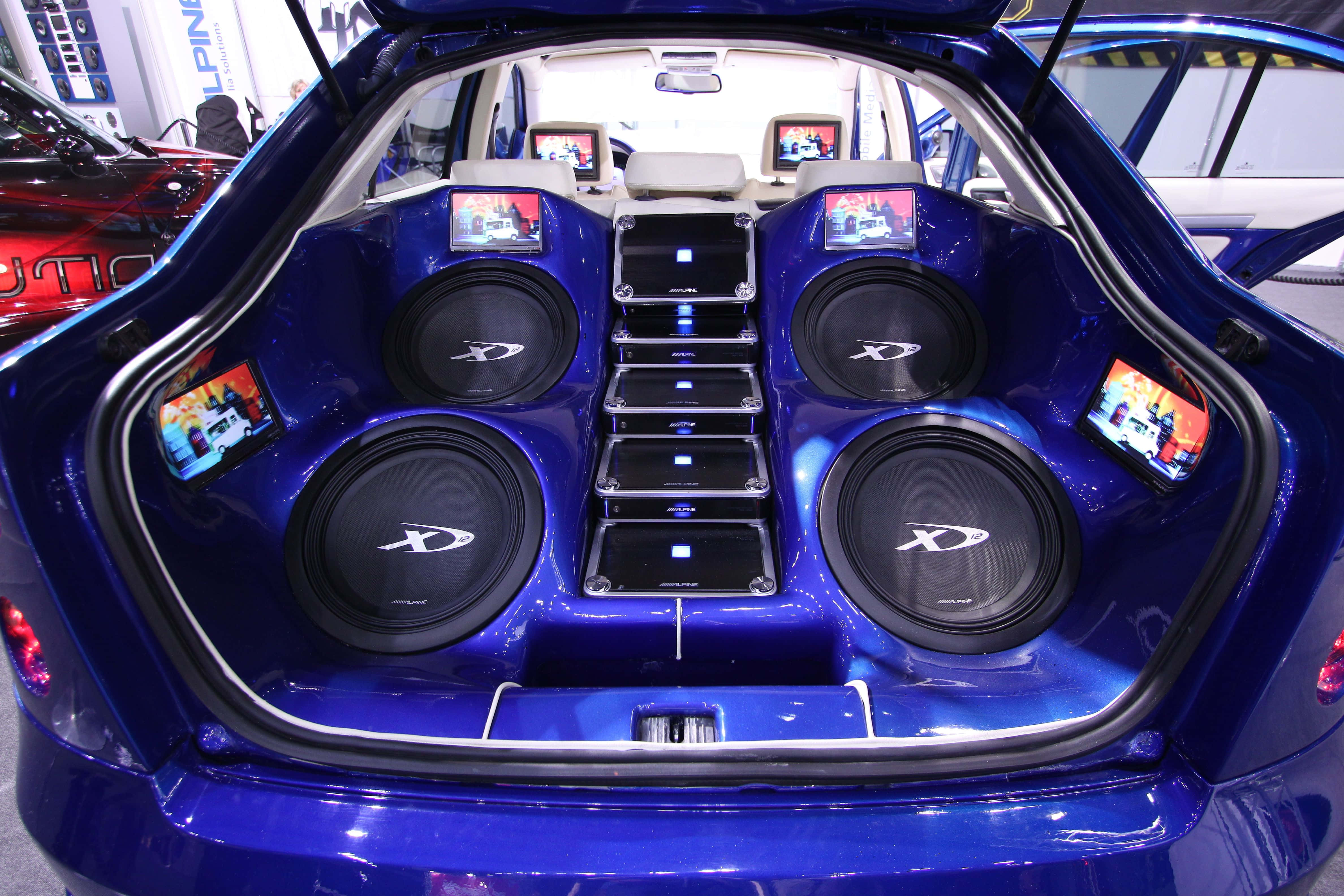 Car Audio 桌布 壁紙 — 一個亮面藍色汽車後車廂，改裝了四個大型超低音揚聲器和多個小型螢幕，顯示汽車音響內容。
