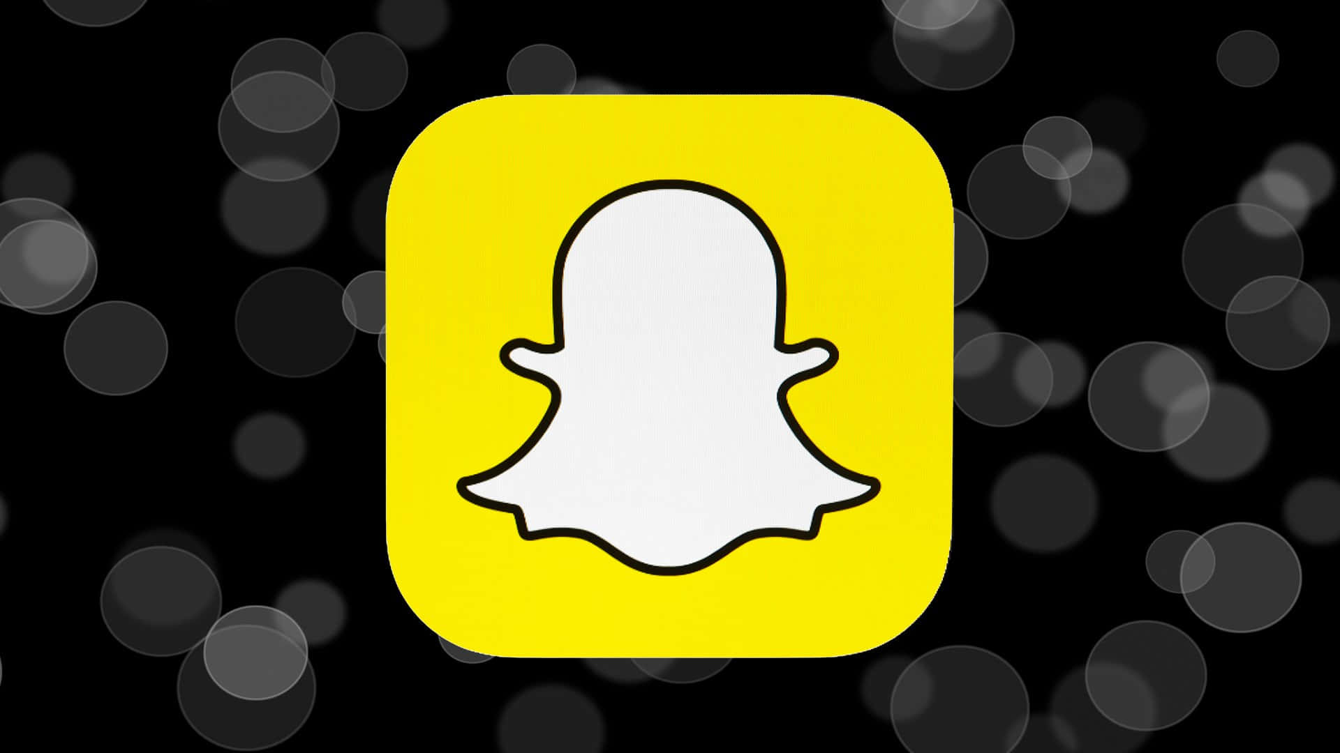 Snapchat 桌布 壁紙 — 一個亮黃色的Snapchat應用程式圖示，中央有一個白色鬼魂標誌，背景為黑色並帶有柔和的灰色散景圓圈。