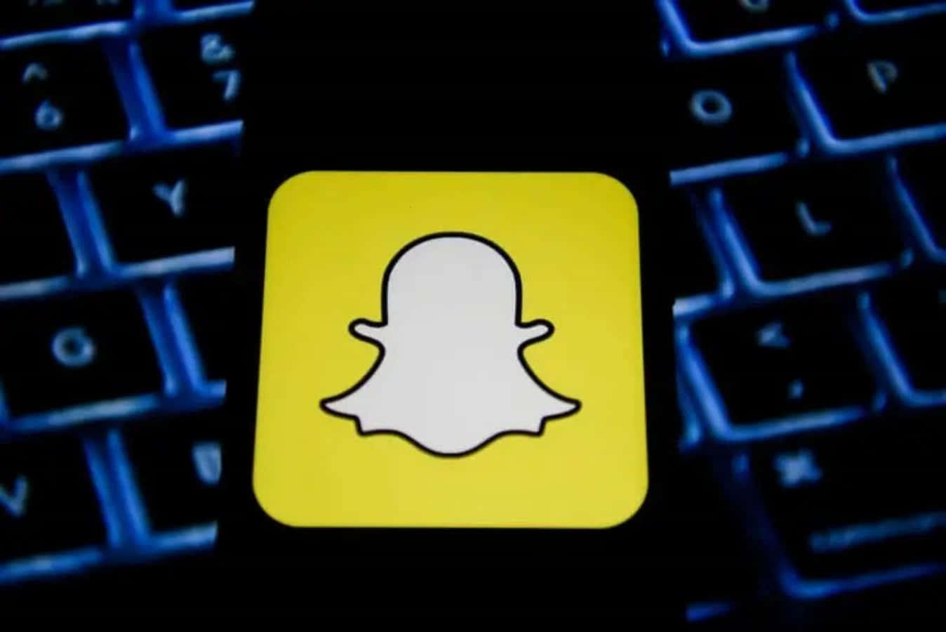 Snapchat 桌布 壁紙 — 一個亮黃色的Snapchat鬼魂標誌，置中在一個有發光藍色背光的深色鍵盤上。