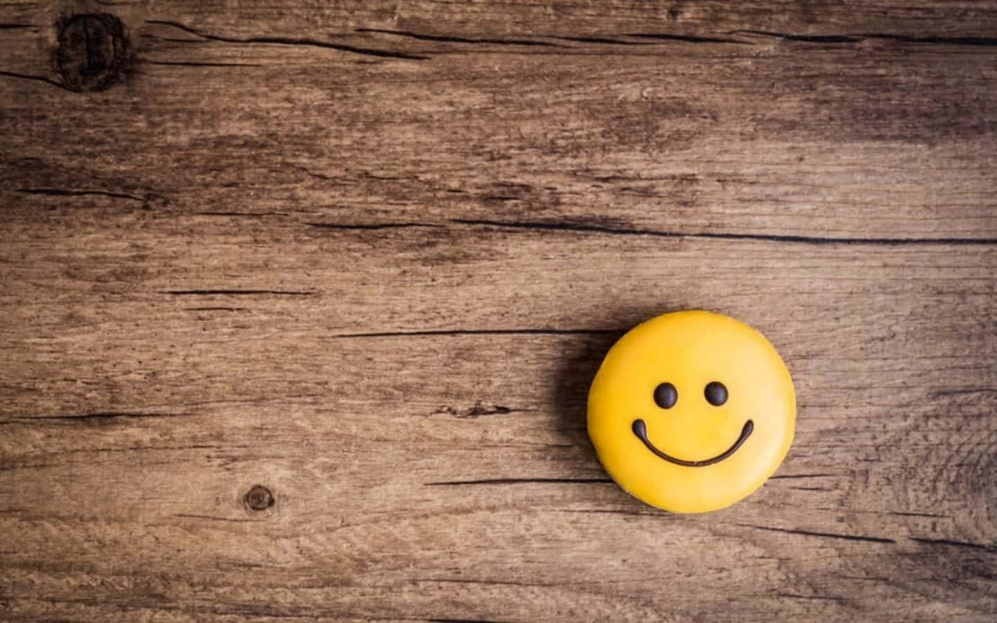 Happy Face 桌布 壁紙 — 一個亮黃色的笑臉按鈕放在一塊紋理和節疤清晰可見的風化木表面上。