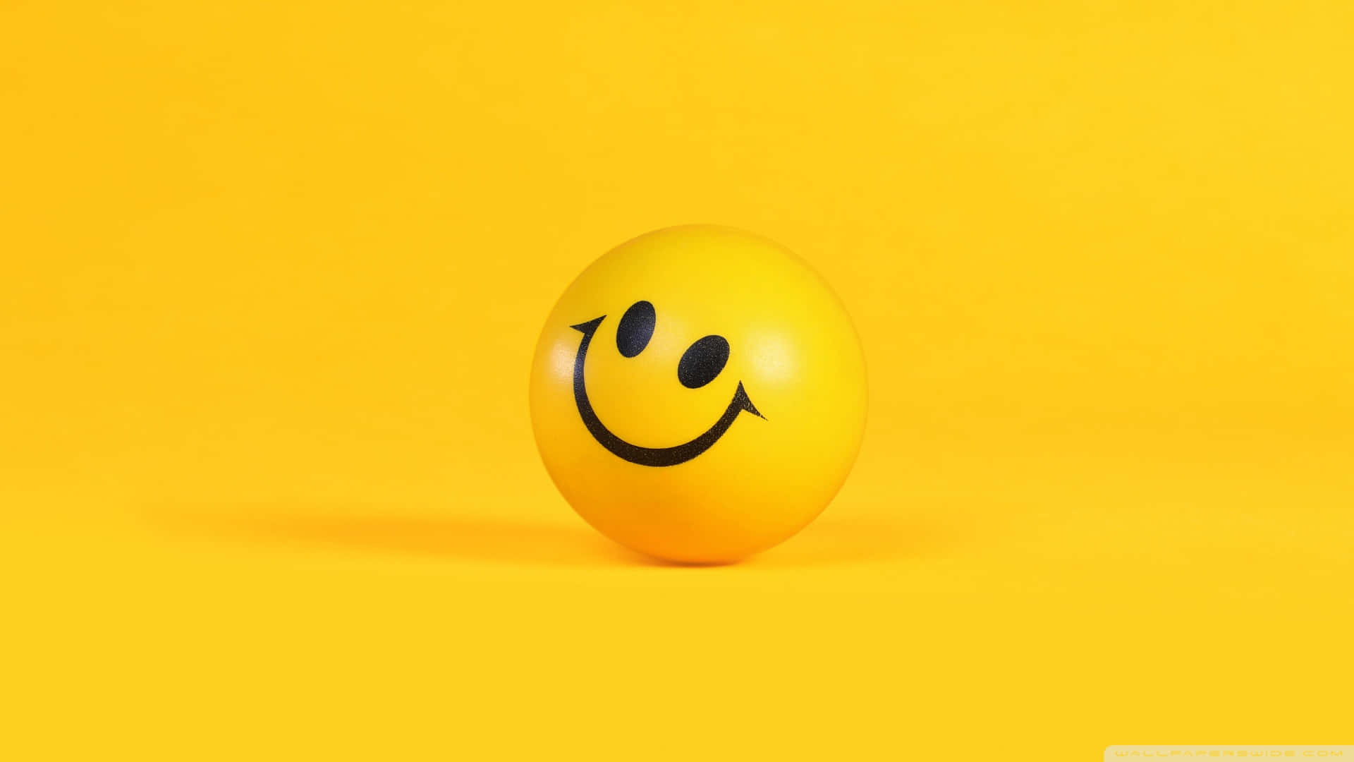 Smiley 桌布 壁紙 — 一個亮黃色的笑臉球放在純黃色背景上，投射出柔和的陰影。