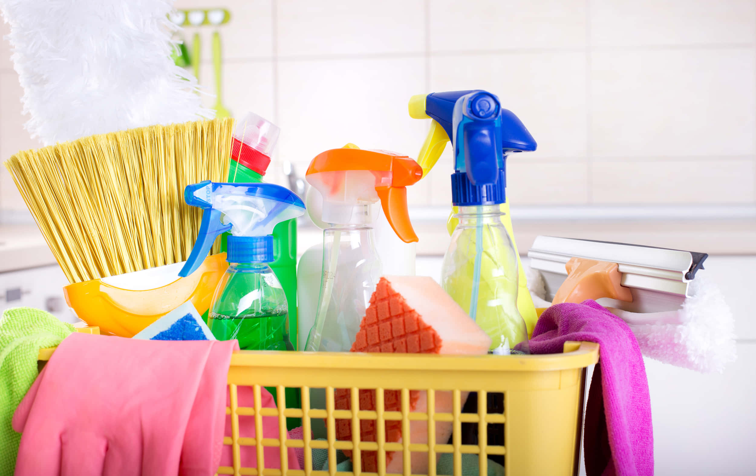 Cleaning 桌布 壁紙 — 一個亮黃色的籃子，裝滿了色彩繽紛的清潔用品，背景是磁磚廚房。