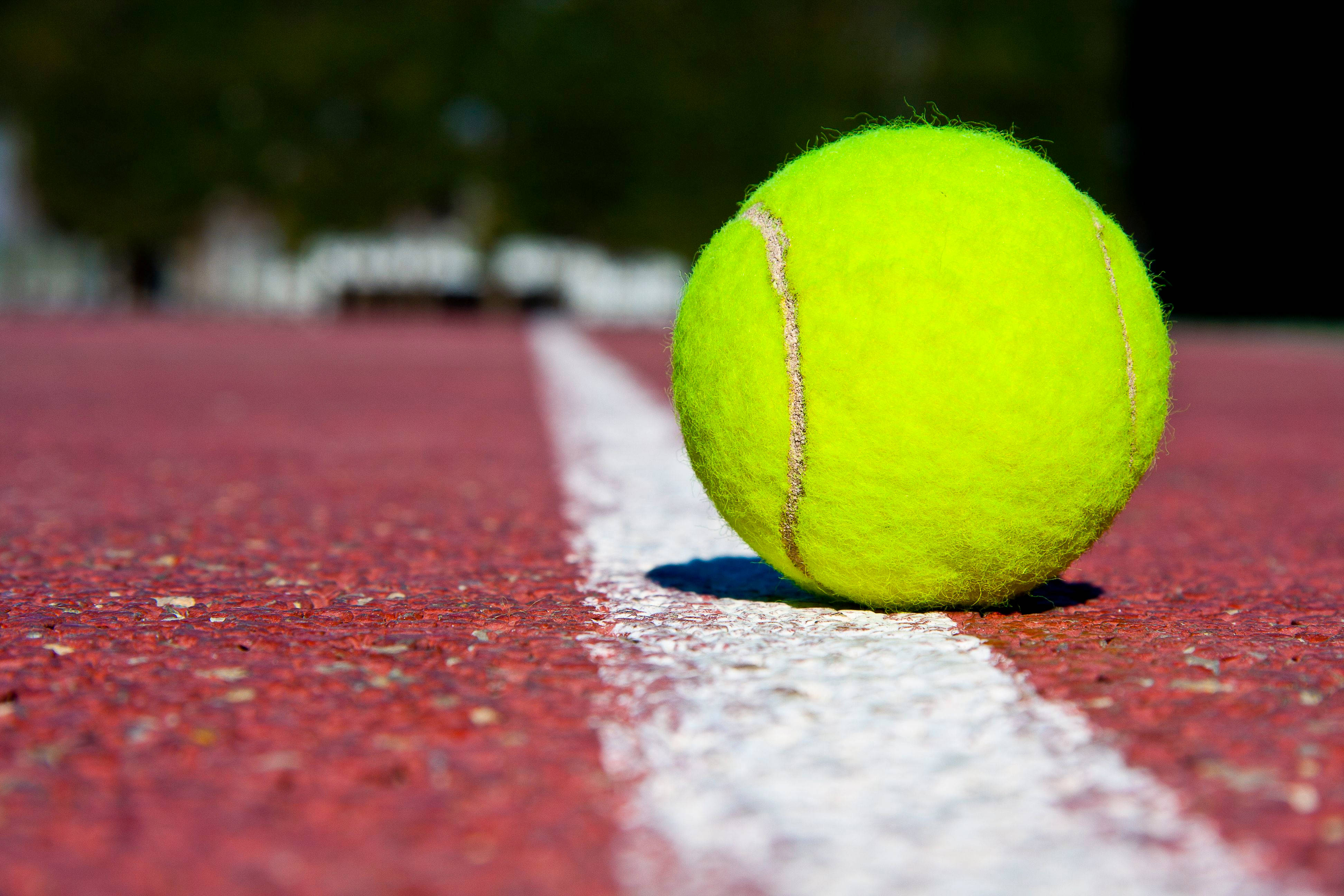 Tennis 桌布 壁紙 — 一個亮黃色的網球在陽光下放在紅色球場的白線旁邊。