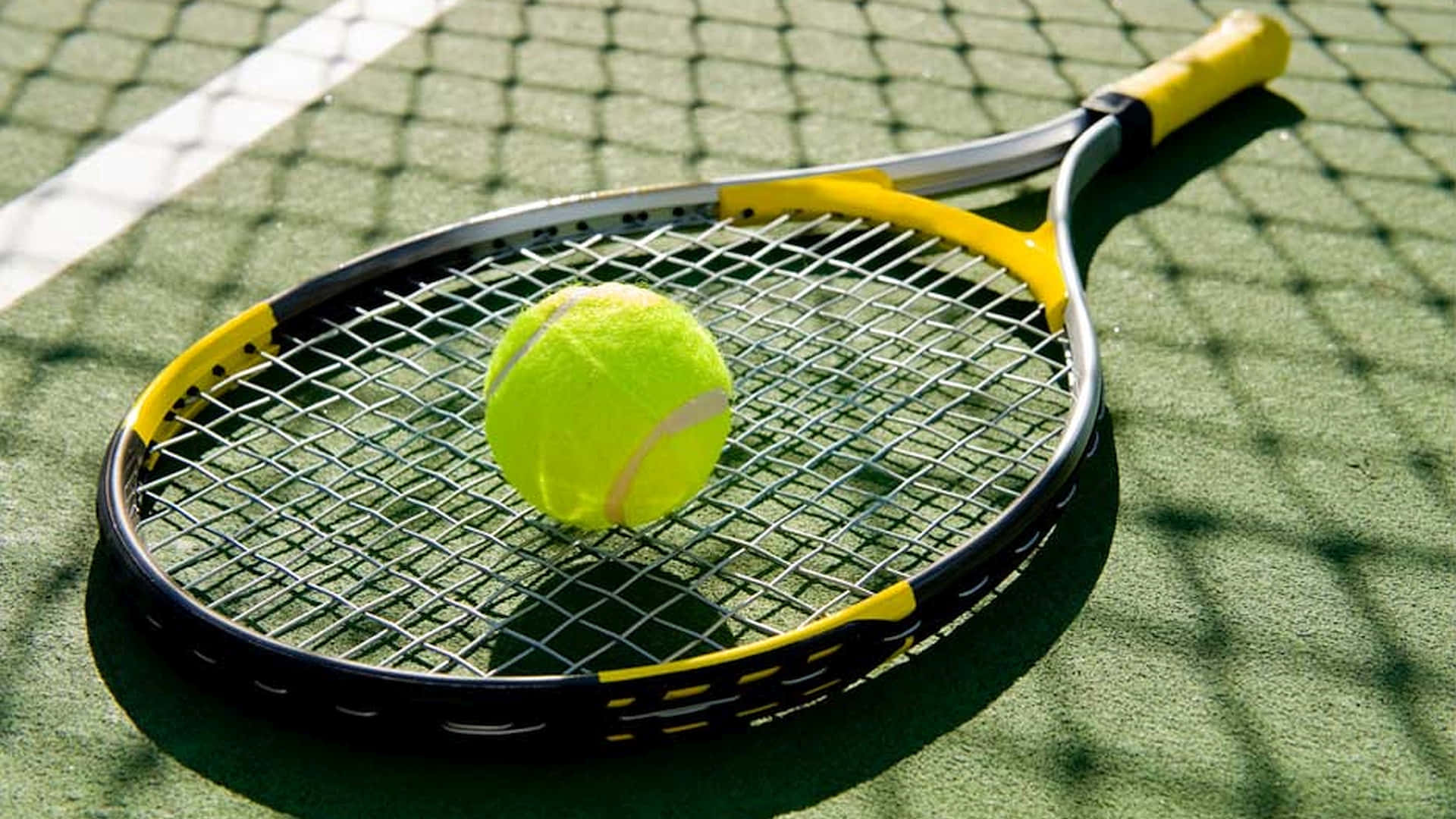 Tennis Ball 桌布 壁紙 — 一個亮黃色的網球放在一個黃黑色的球拍上，球拍躺在強烈陽光下的綠色球場上。