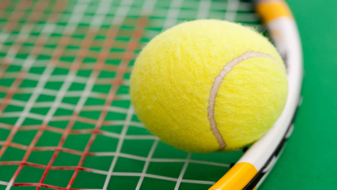 720p Tennis 桌布 壁紙 — 一個亮黃色的網球放在球拍的弦上，背景是綠色的球場。
