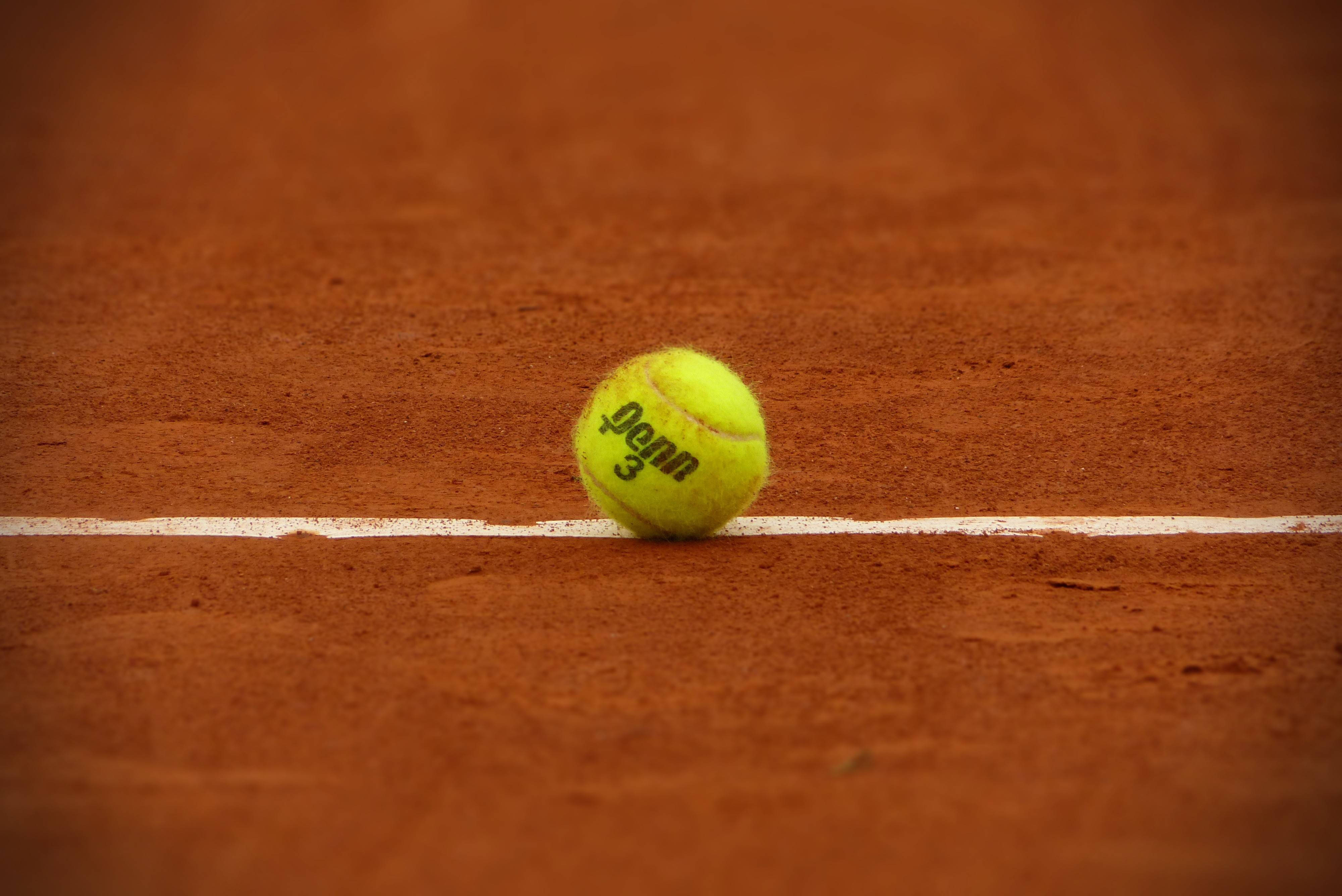 Tennis 桌布 壁紙 — 一個亮黃色的網球放在紅土球場的白色線上，球場表面呈紋理紅褐色。