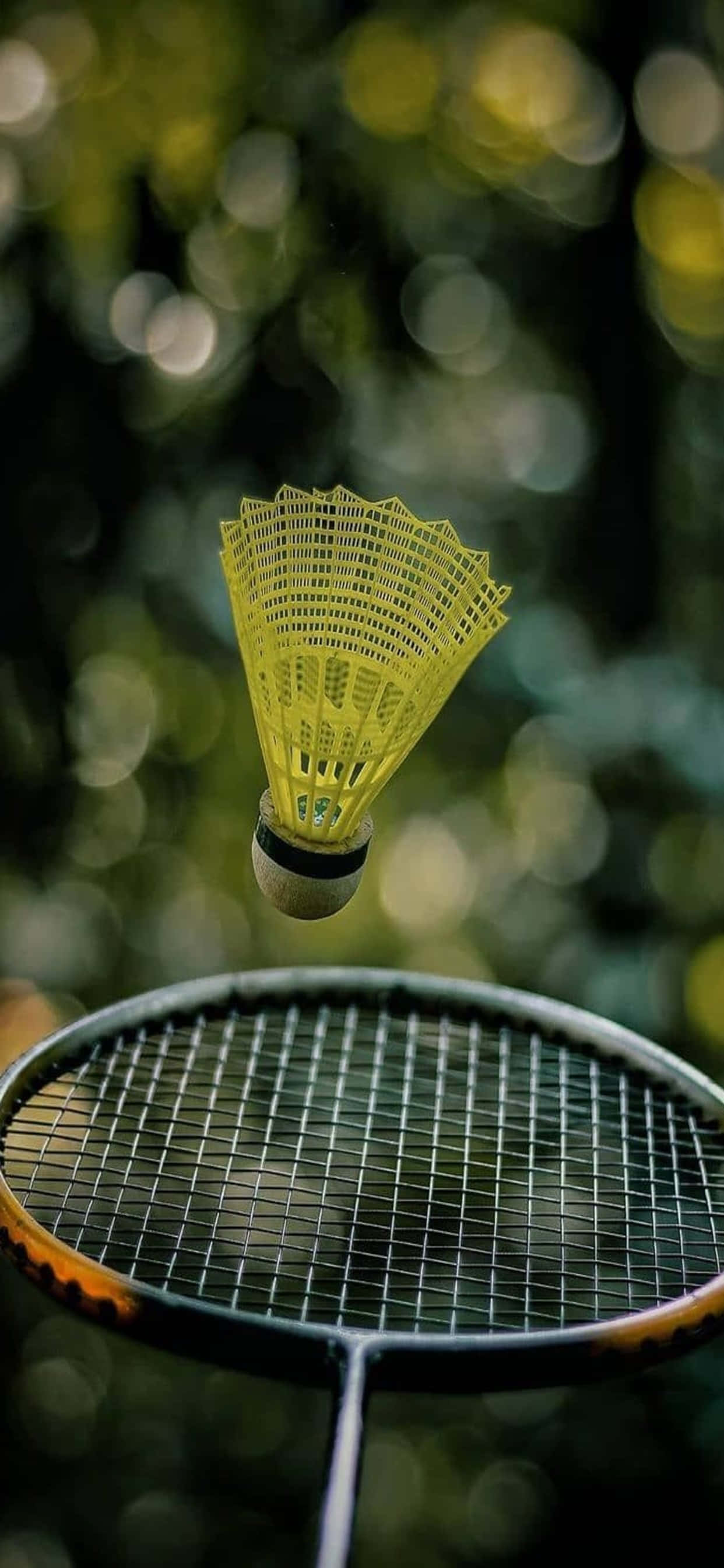 iPhone Xs Max Badminton 桌布 壁紙 — 一個亮黃色的羽毛球在球拍上方盤旋，背景是柔和的綠色散景。