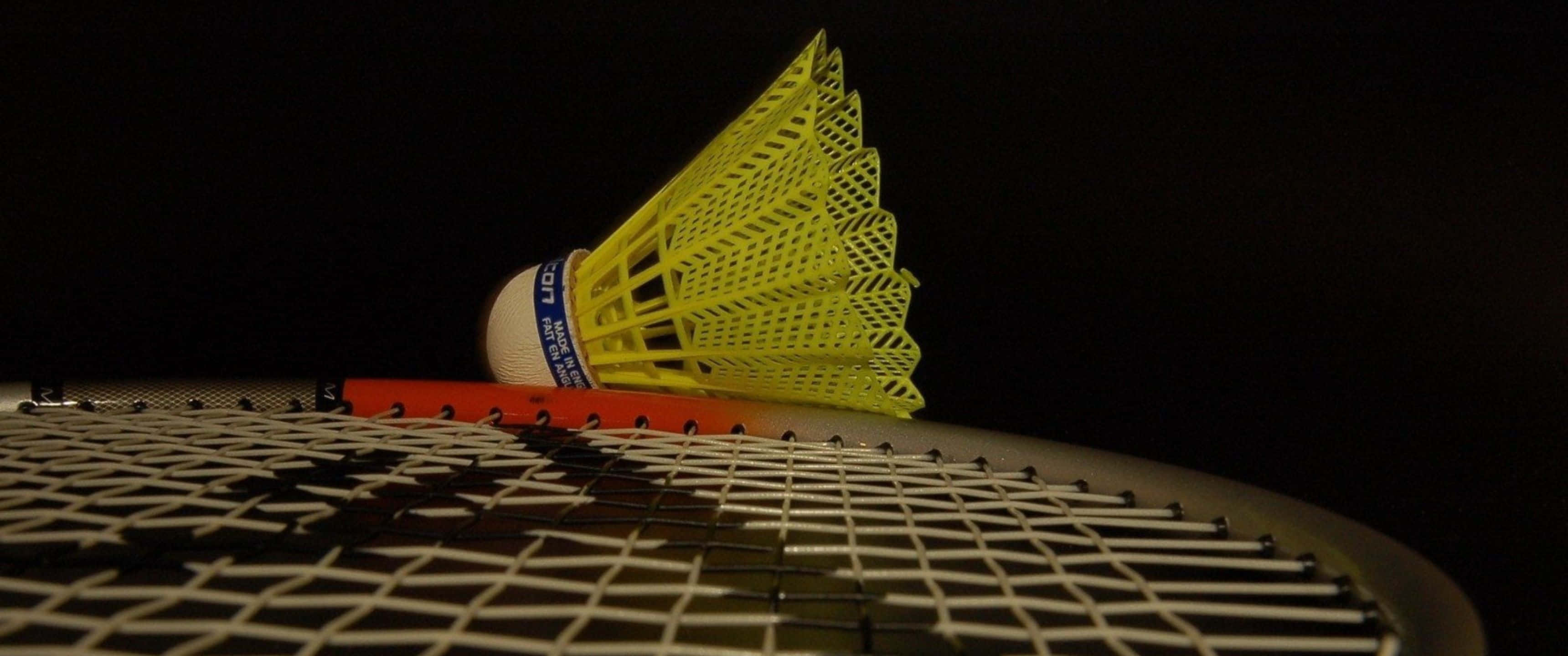 3440x1440p Badminton 桌布 壁紙 — 一個亮黃色的羽毛球放在深色背景的羽毛球拍上。