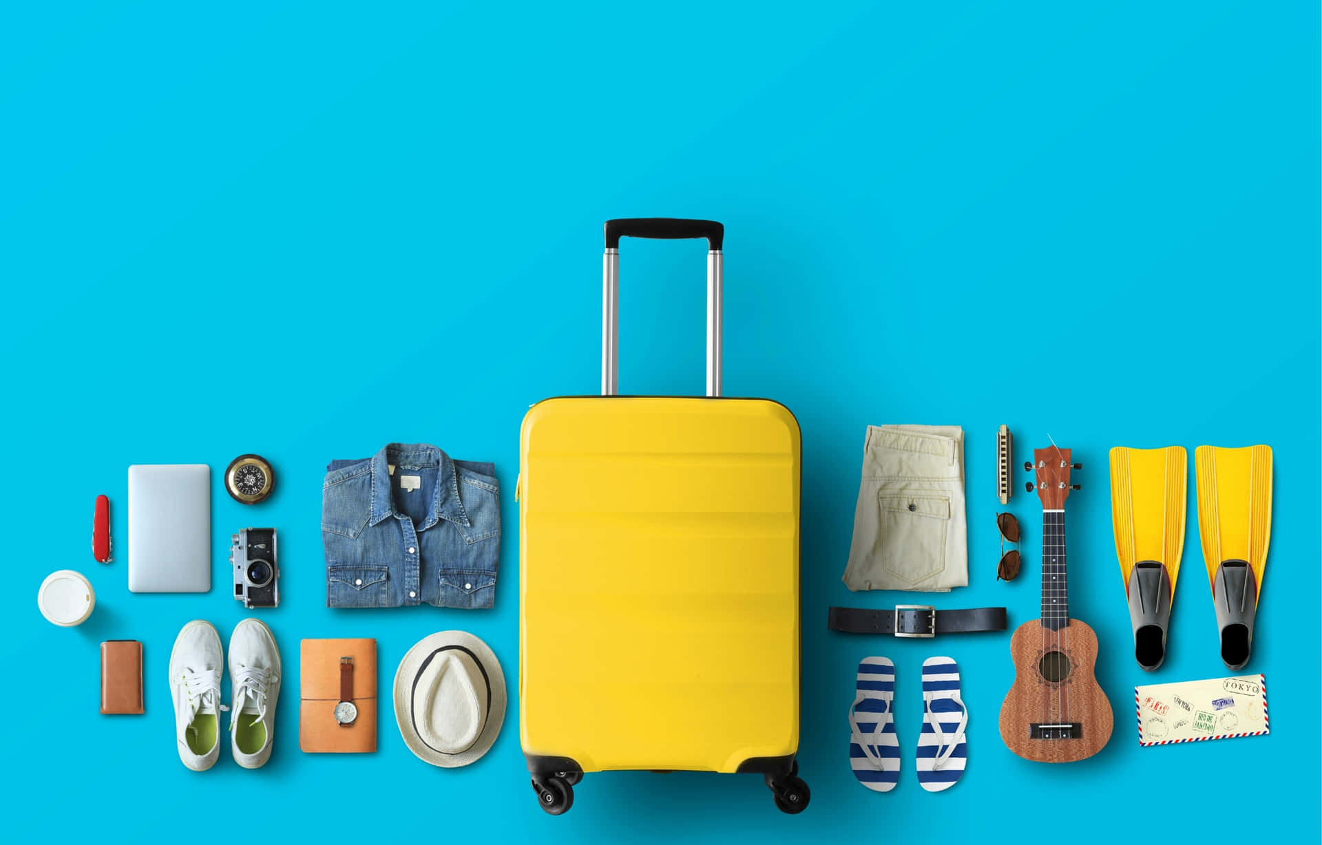 Travel Packing Flatlay With Yellow Suitcase 壁紙 — 一個亮黃色行李箱置於鮮豔藍色背景中央，周圍環繞著旅行裝備，包括人字拖、烏克麗麗和潛水蛙鞋。