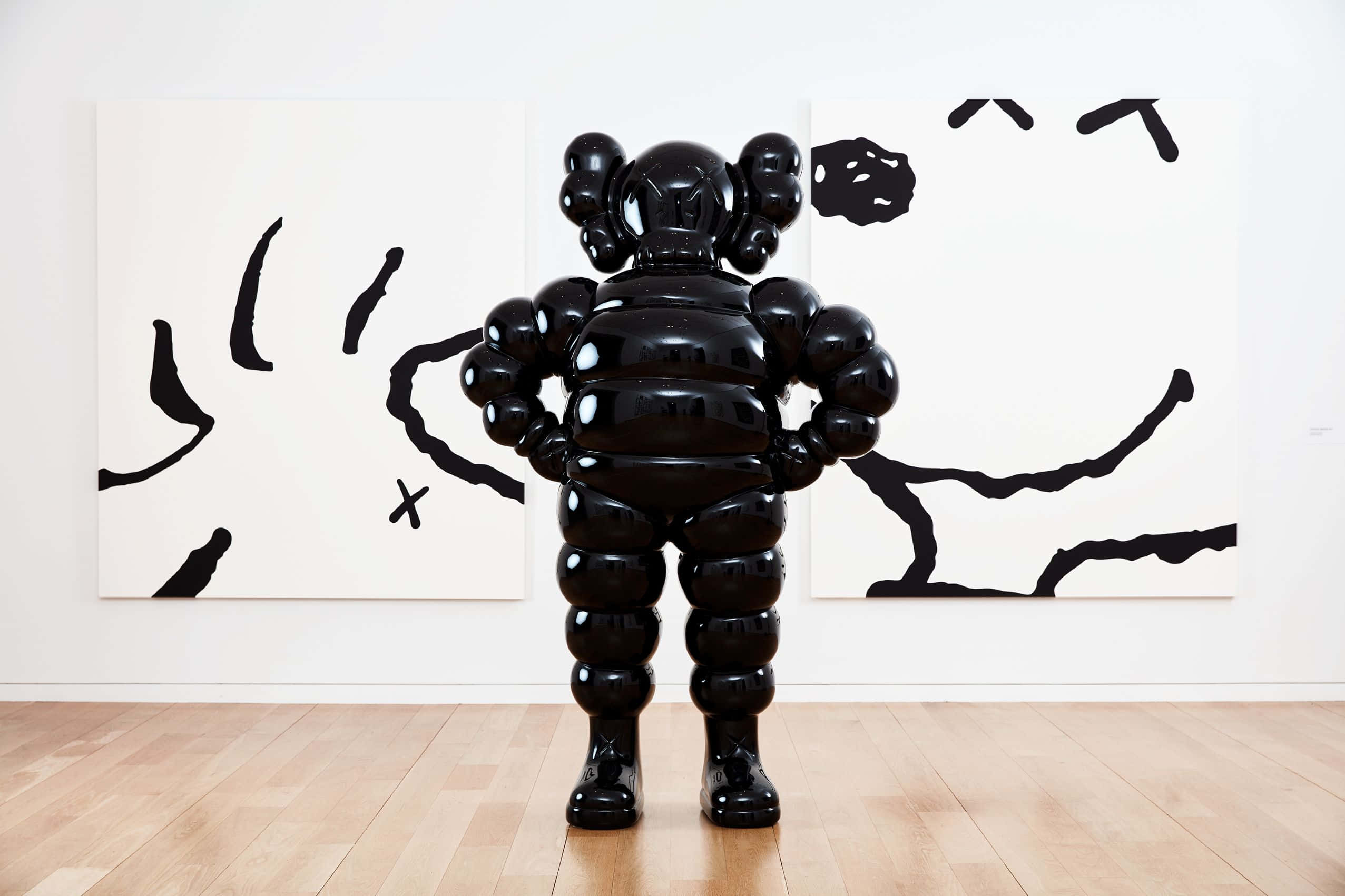 KAWS 桌布 壁紙 — 一個亮黑色的KAWS Companion雕像雙手叉腰，面向極簡主義畫廊中的抽象黑色畫作。