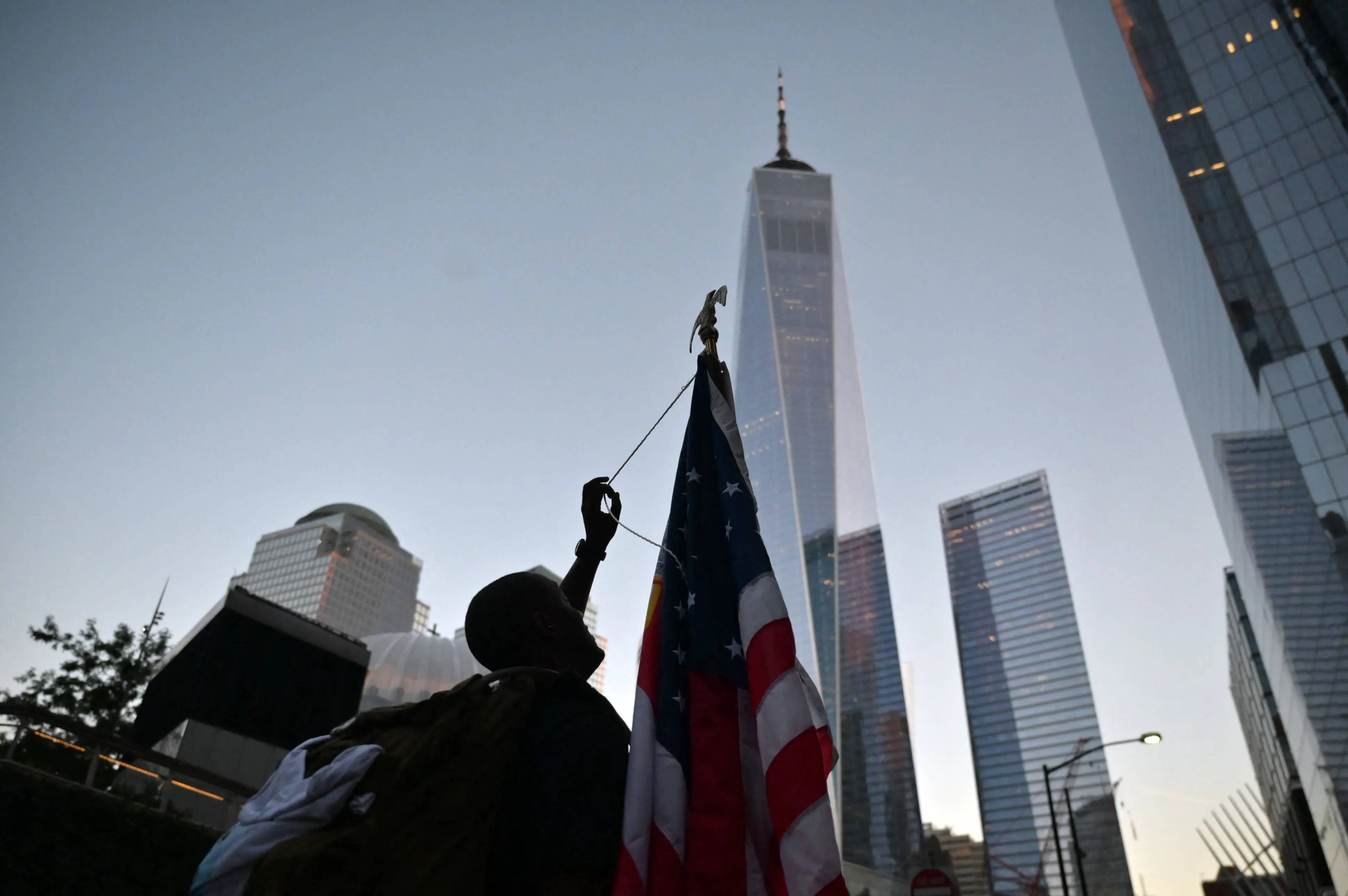 911 Memorial 桌布 壁紙 — 一個人以暮色天空為剪影，在紐約市高聳的世貿中心一號樓前手持美國國旗。