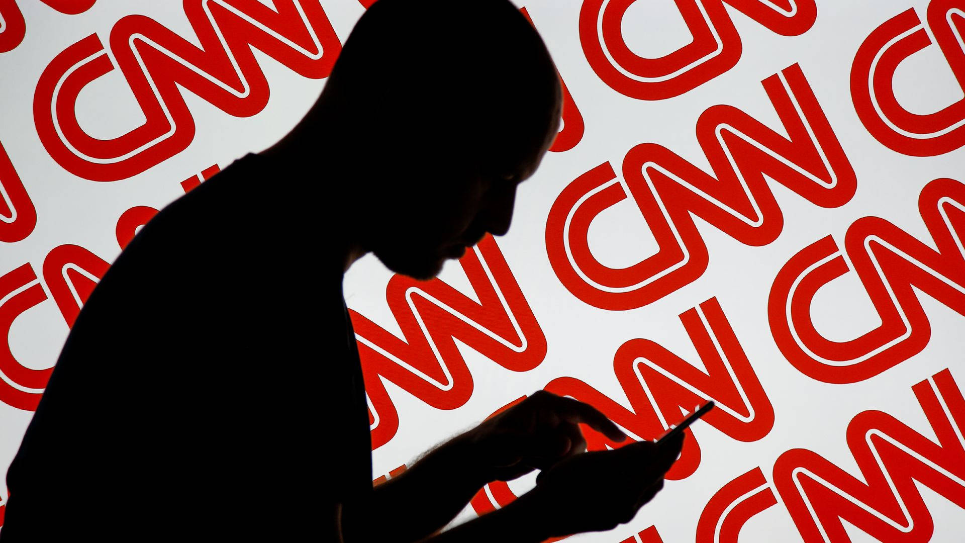 Cnn 桌布 壁紙 — 一個人使用電話的剪影，背景是重複的紅色CNN標誌。