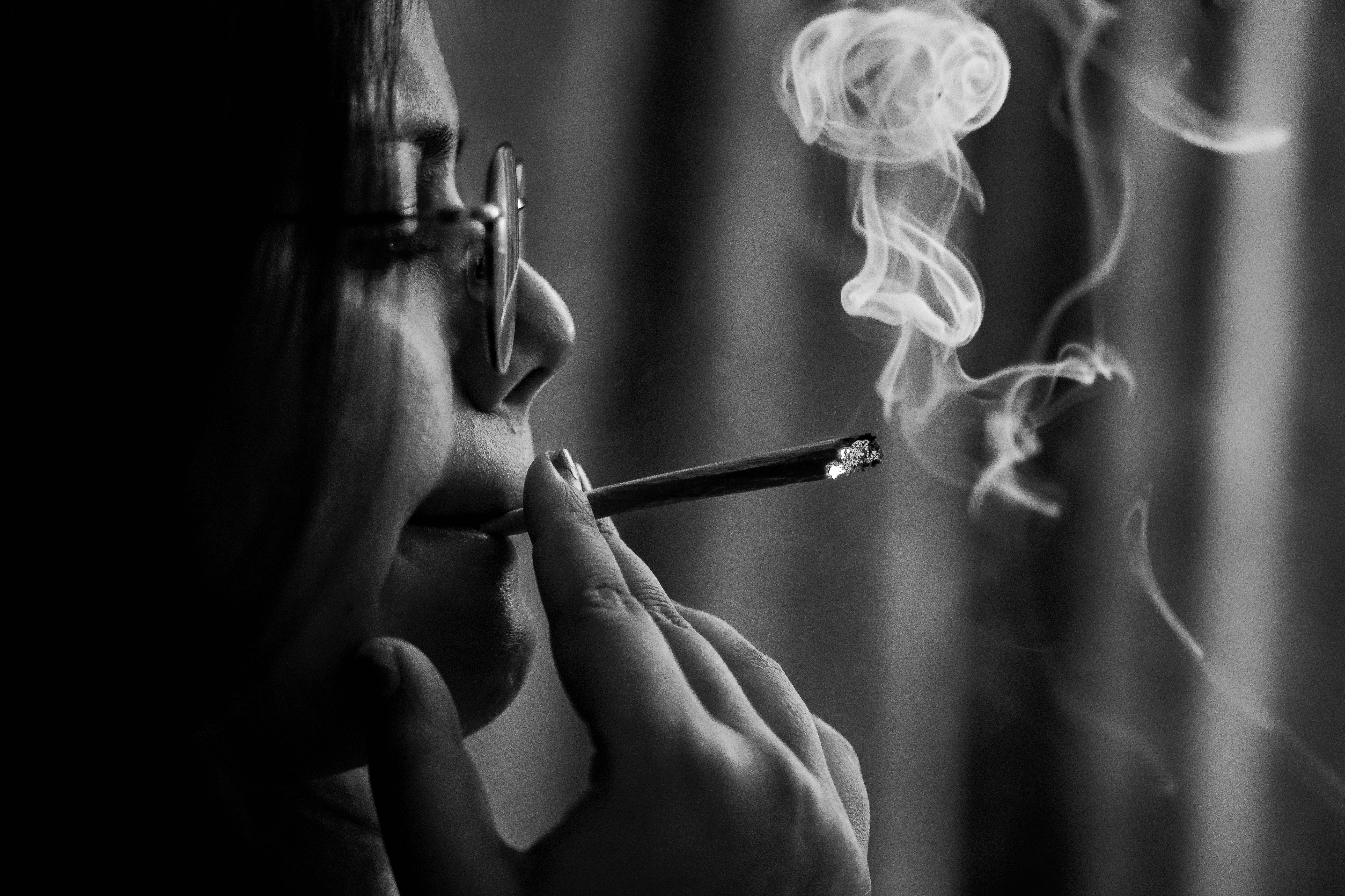 吸大麻 桌布 壁紙 — 一個人側面抽煙，煙霧向上繚繞，背景是模糊的窗簾，呈單色調。