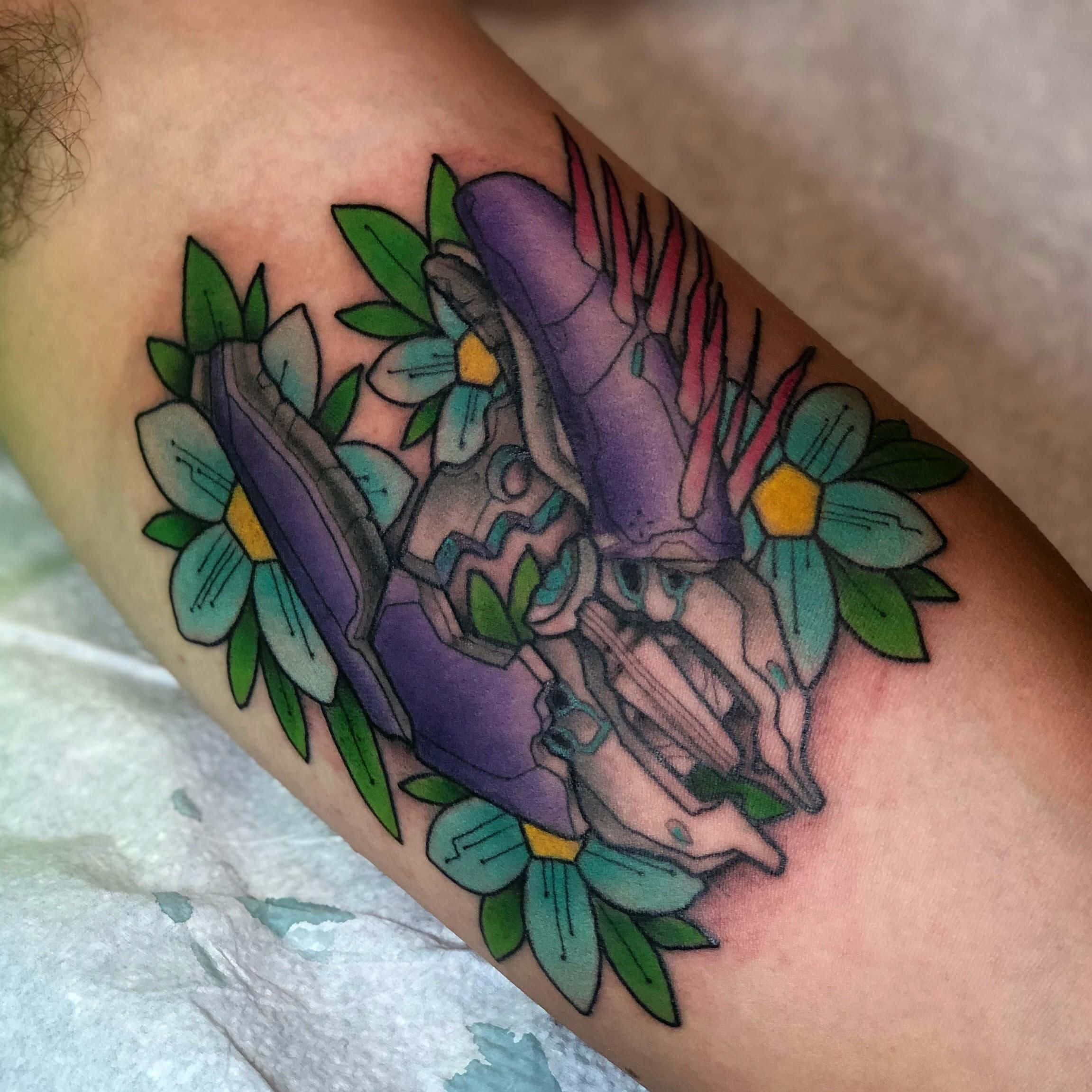 Halo Needler 桌布 壁紙 — 一個人前臂上的紫色機械臂紋身，周圍環繞著青綠色花朵和綠色葉子，色彩鮮豔。