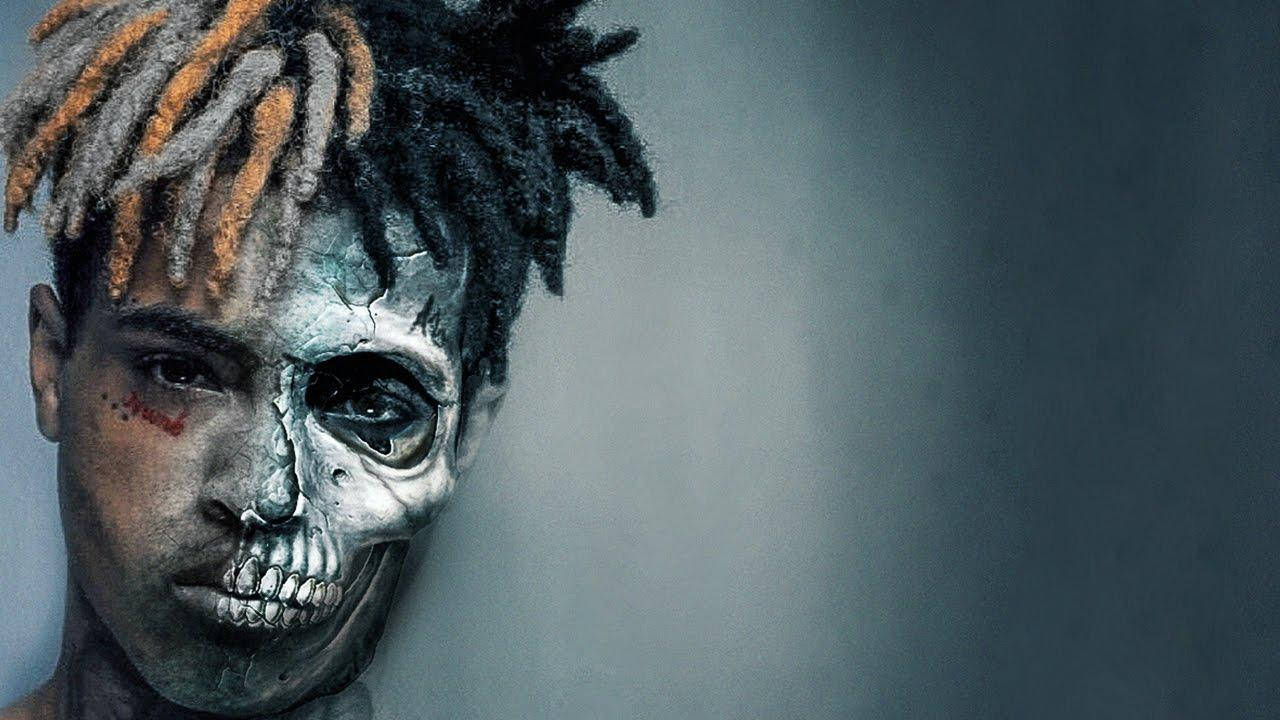 Xxxtentacion Cartoon 桌布 壁紙 — 一個人化著半邊骷髏妝，留著橙色髮尾的辮子頭，在柔和的灰色背景下凝視著。