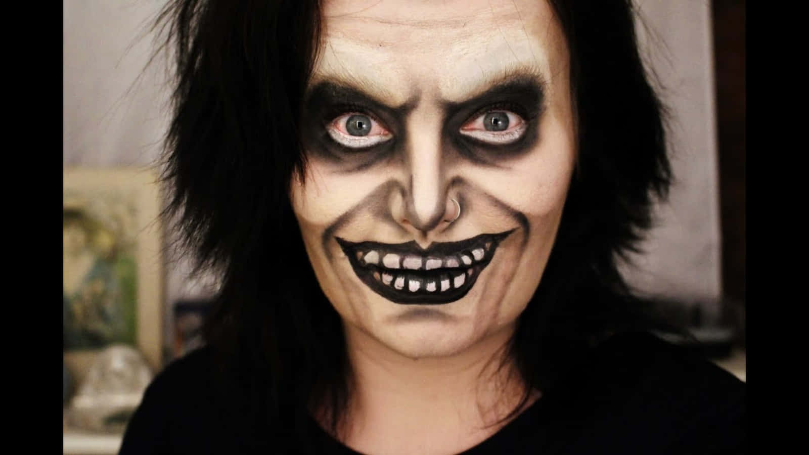 Scary Face 桌布 壁紙 — 一個人化著戲劇性的哥德妝容，蒼白的皮膚、黑色眼妝和露齒咧嘴笑，強烈地凝視著鏡頭。