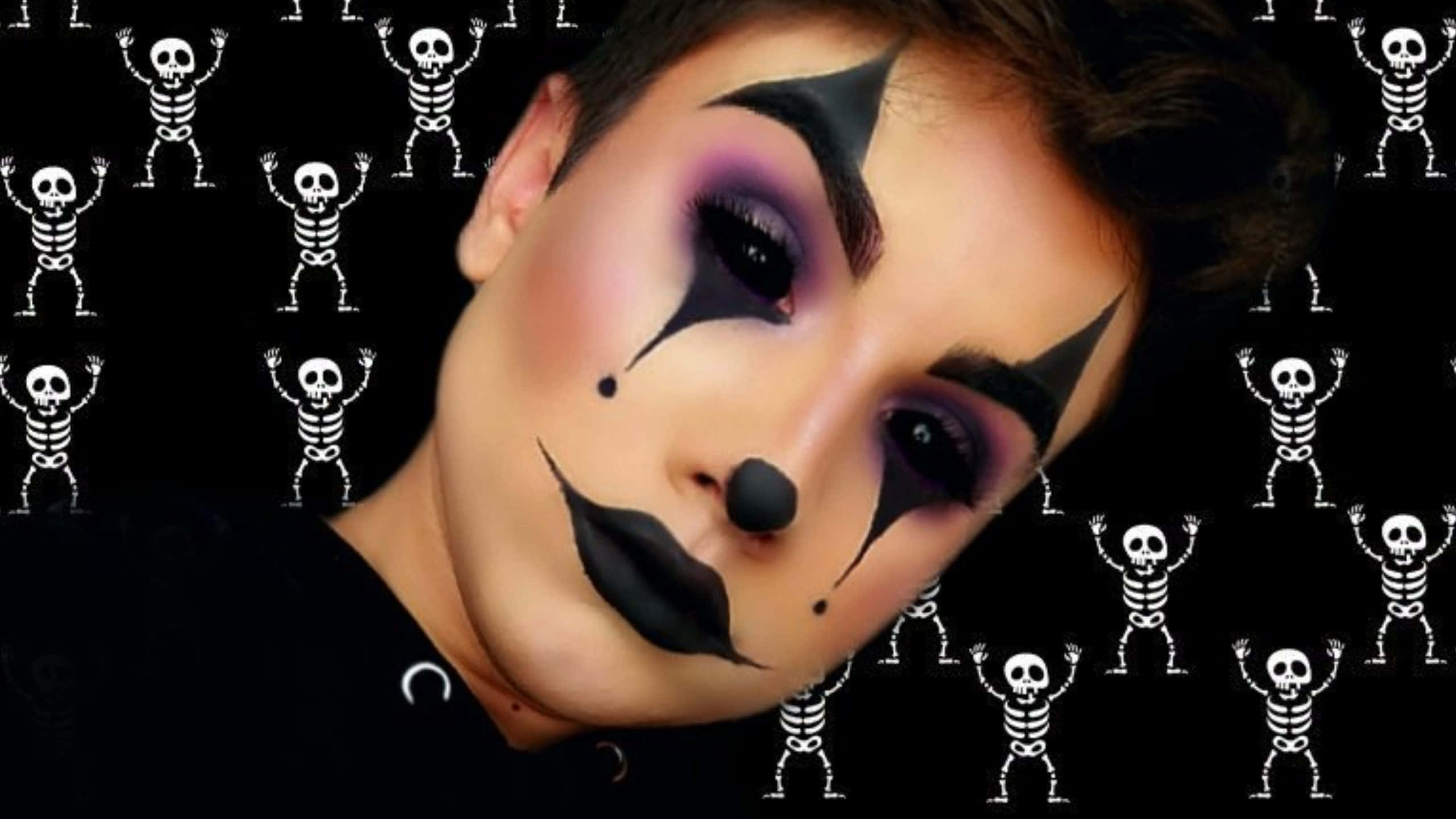 Halloween Makeup 桌布 壁紙 — 一個人化著戲劇性的黑紫色小丑妝，在充滿白色跳舞骷髏圖案的黑色背景前擺姿勢。