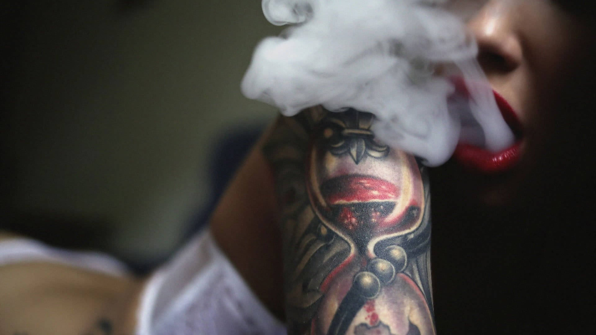 Tattoo 桌布 壁紙 — 一個人呼出濃厚白色蒸氣，同時展示帶有紅色嘴唇和華麗圖案的詳細紋身前臂。