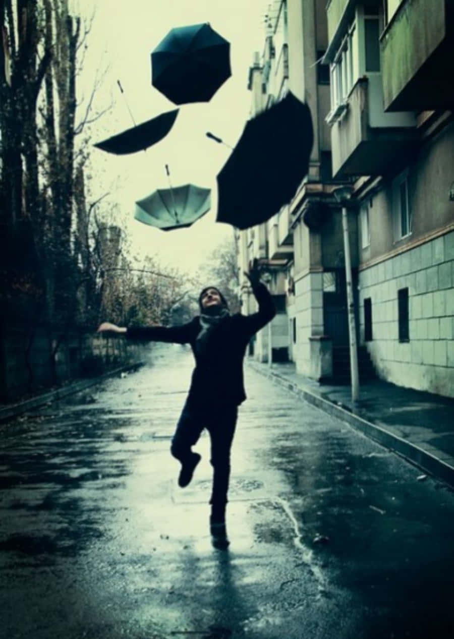 復古 桌布 壁紙 — 一個人在下雨的城市小巷中歡快地跳躍，多把黑色雨傘戲劇性地漂浮在他們周圍。