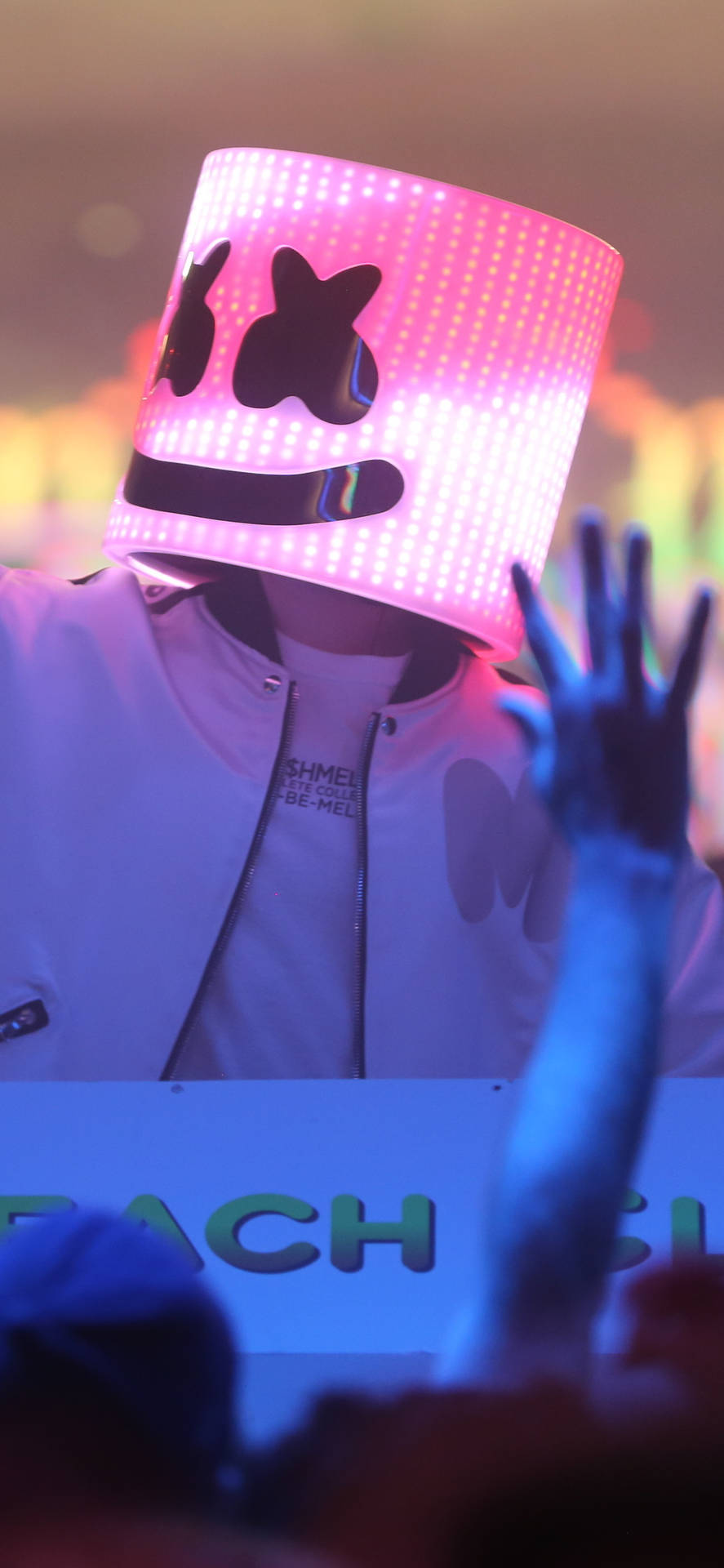 Marshmello 動態圖 桌布 壁紙 — 一個人在充滿活力的演唱會中戴著發光的粉紅色LED Marshmello頭盔，舉起雙手，周圍是五彩繽紛的燈光。