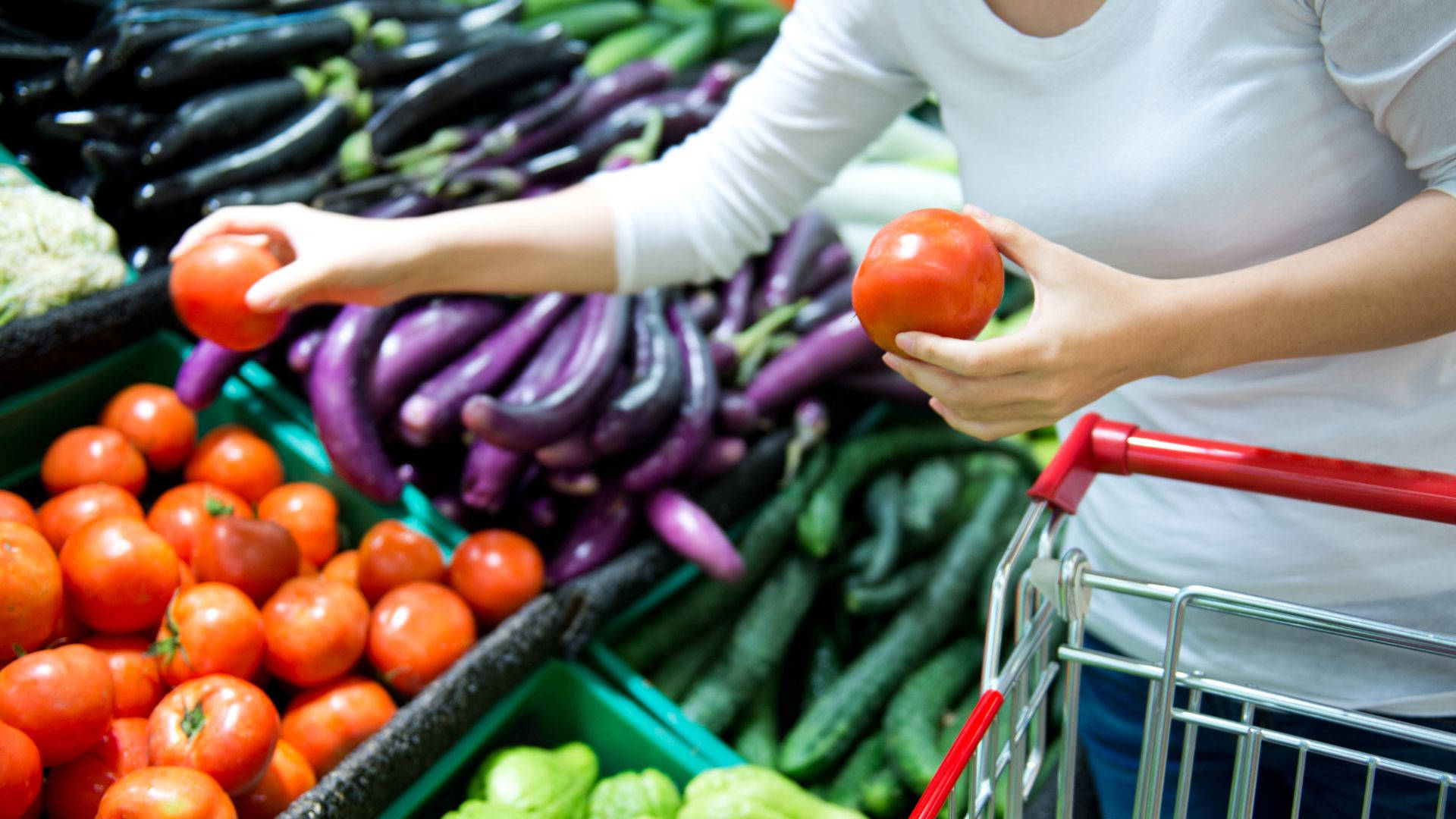 Vegetables 桌布 壁紙 — 一個人在充滿茄子和黃瓜的新鮮蔬果通道挑選新鮮紅色番茄。