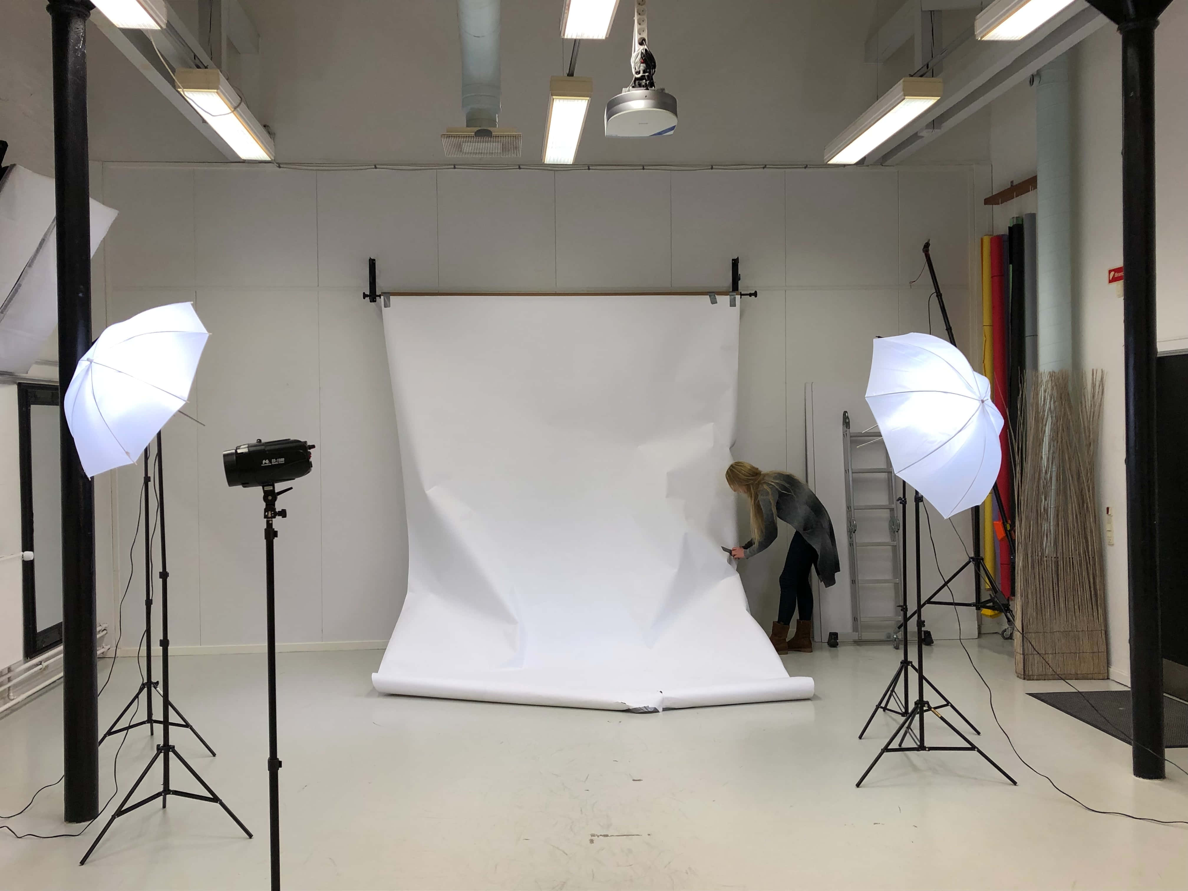 Photography Studio 桌布 壁紙 — 一個人在光線充足的攝影棚內調整大型白色背景，周圍是專業照明設備。